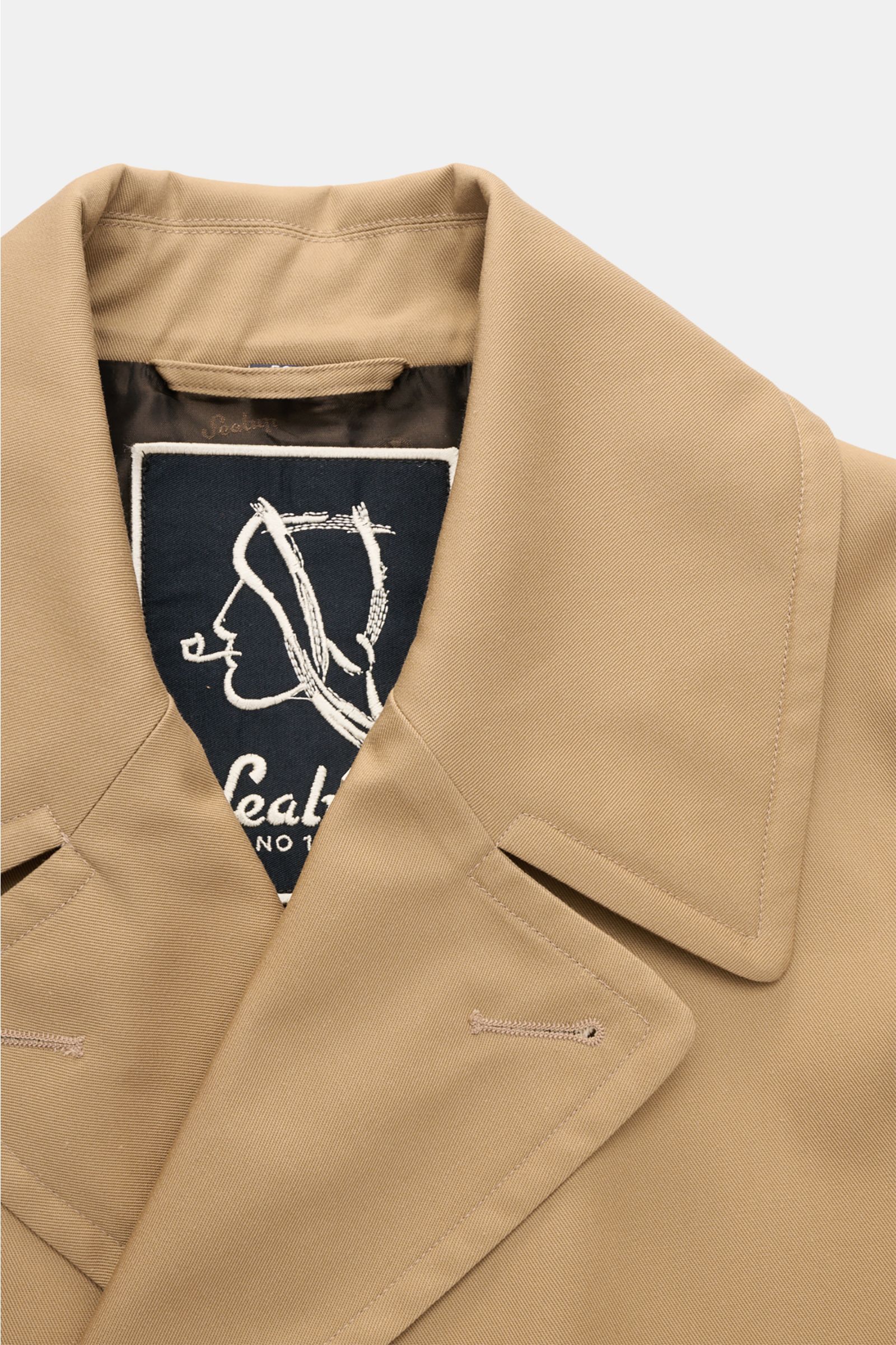 Close-up front view of the Sealup Pea coat 'Amalfi' beige collar showing fine twill fabric, wide lapel collar, and inner logo lining. Get the look of a Hanseatic merchant with the elegant pea coat 'Amalfi' by traditional label SEALUP: made of lightweight 