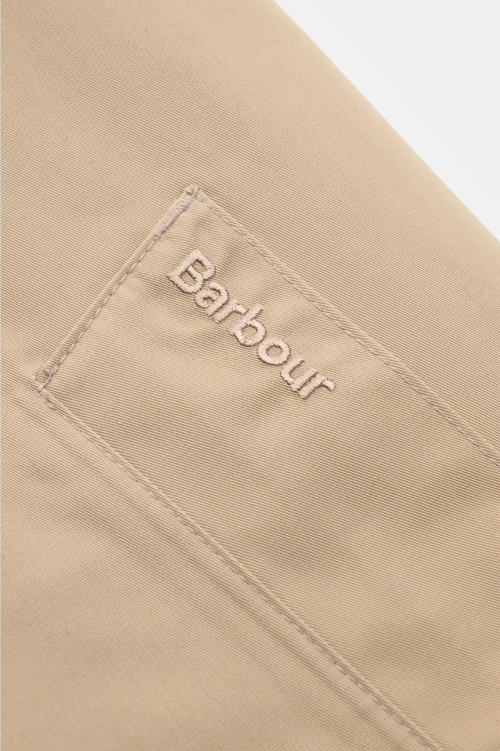 Close-up front view of Barbour Rain coat 'Rokig' beige showing embroidered logo on high-quality microfibre fabric with waterproof coating.