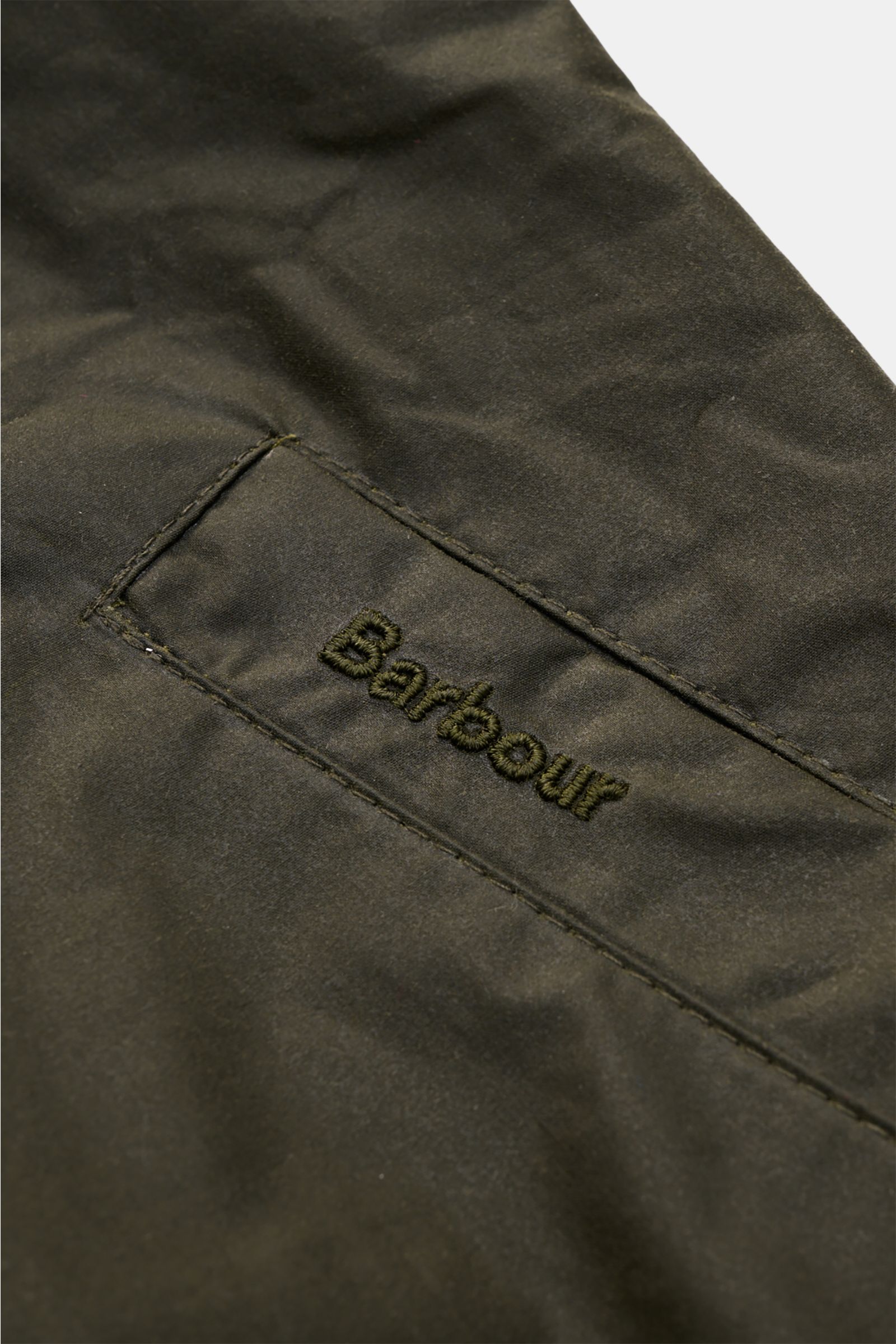Close-up detail of the Barbour Waxed blouson 'Royston' dark olive showing the embroidered logo on waxed cotton fabric, photographed from above.

Classic blouson by traditional label BARBOUR: With its short cut and signature corduroy trim on the collar,