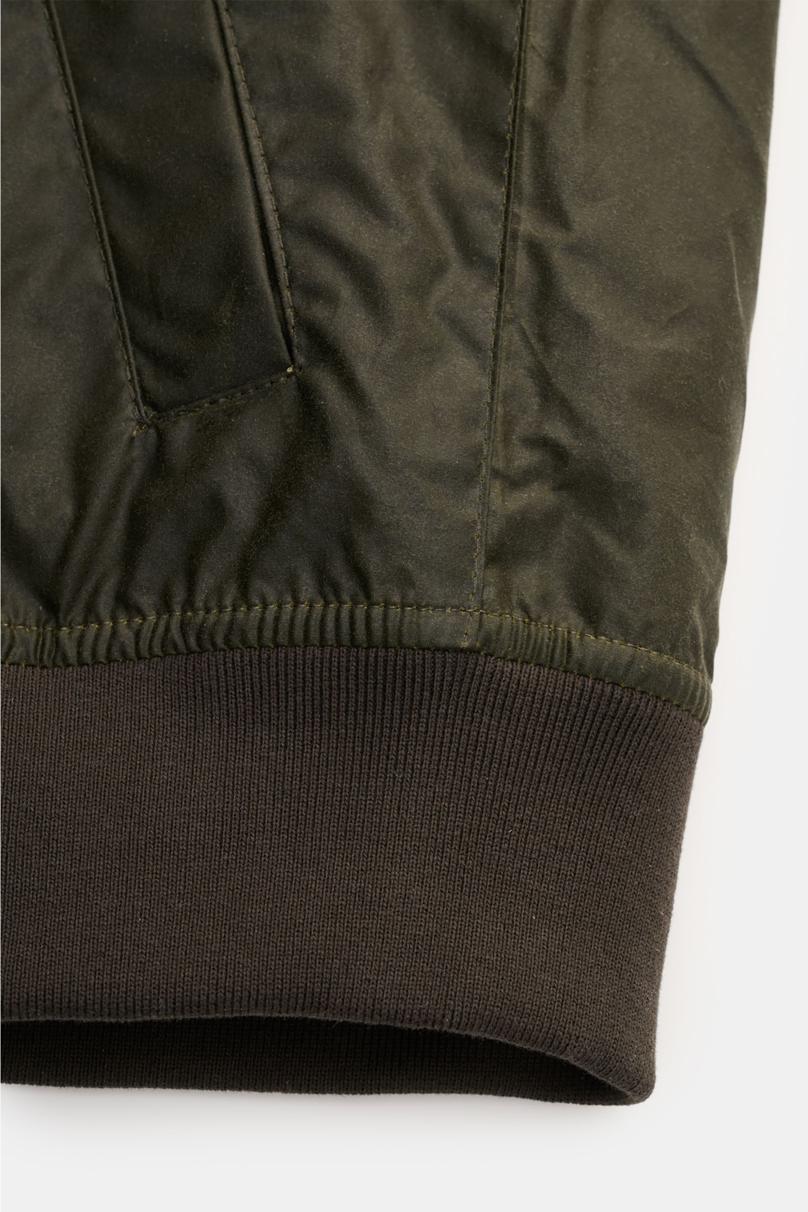 Close-up front view of the elasticated hem and slanted hip pocket on the Barbour Waxed blouson 'Royston' dark olive, made of waxed cotton.

Description: Classic blouson by traditional label BARBOUR: With its short cut and signature corduroy trim on the