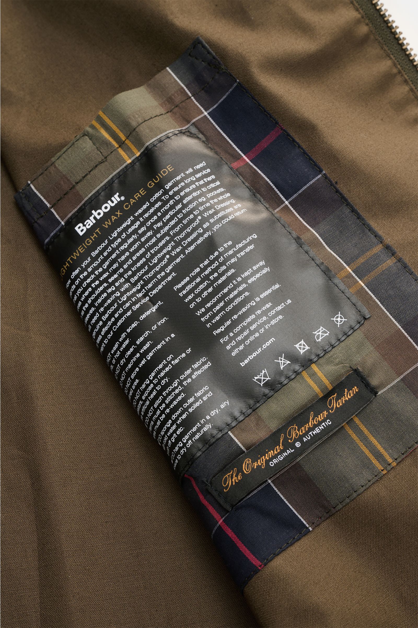 Close-up inside view of Barbour Waxed blouson 'Royston' dark olive showing the lightweight wax care guide label and original Barbour Tartan lining.

Description: 
Classic blouson by traditional label BARBOUR: With its short cut and signature corduroy t