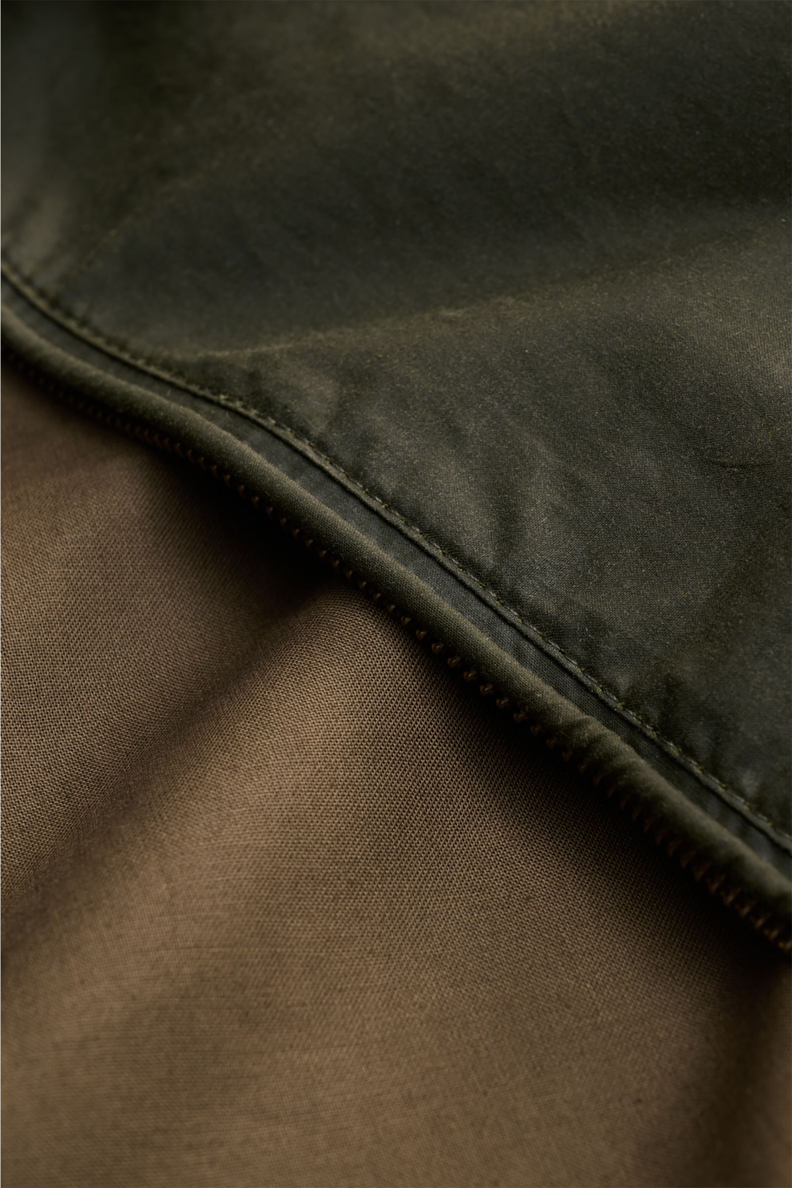 Close-up detail of the Barbour Waxed blouson 'Royston' dark olive showing the waxed cotton outer fabric and the cotton lining, photographed from a top-down perspective.

Classic blouson by traditional label BARBOUR: With its short cut and signature cor