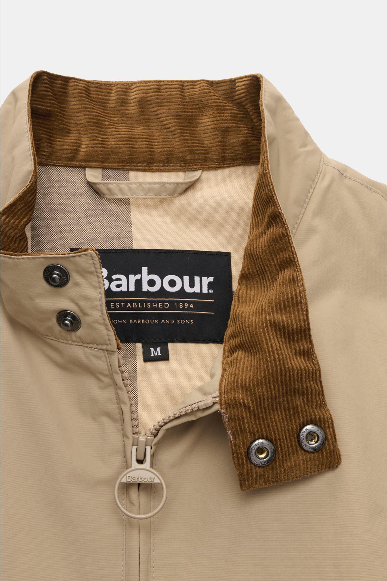 Close-up front view of the Barbour Blouson 'Royston' beige jacket showing its beige microfiber fabric, standing collar with brown corduroy trim and snap buttons, two-way zip with round Barbour-branded pull, and visible inner mesh lining. 

Modern blous