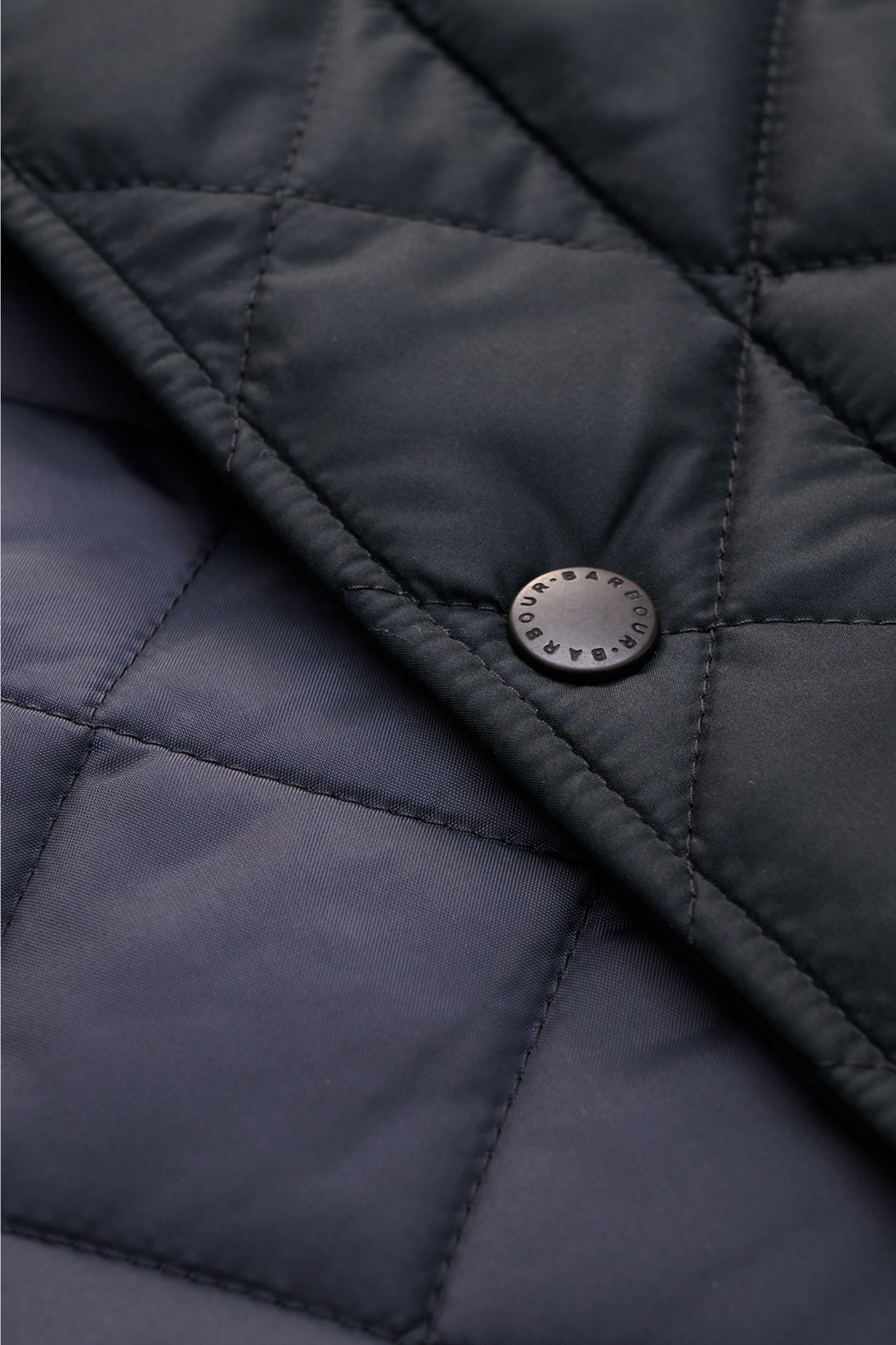 Close-up front detail of Barbour Quilted jacket 'Chelsea Sportsquilt' dark navy showing quilted microfiber, snap button with logo, photographed from above.