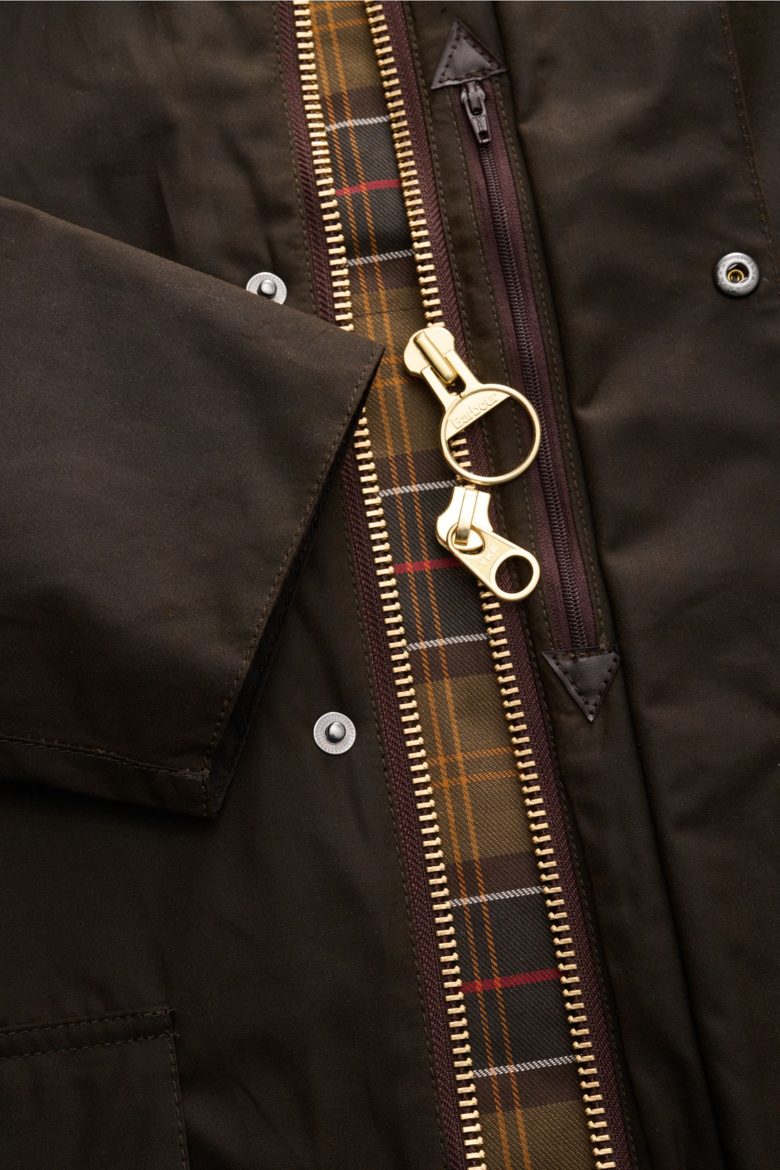 Close-up front view of Barbour Waxed jacket 'Beaufort' dark olive showing waxed cotton fabric, gold two-way zip, snap buttons, and classic tartan lining.