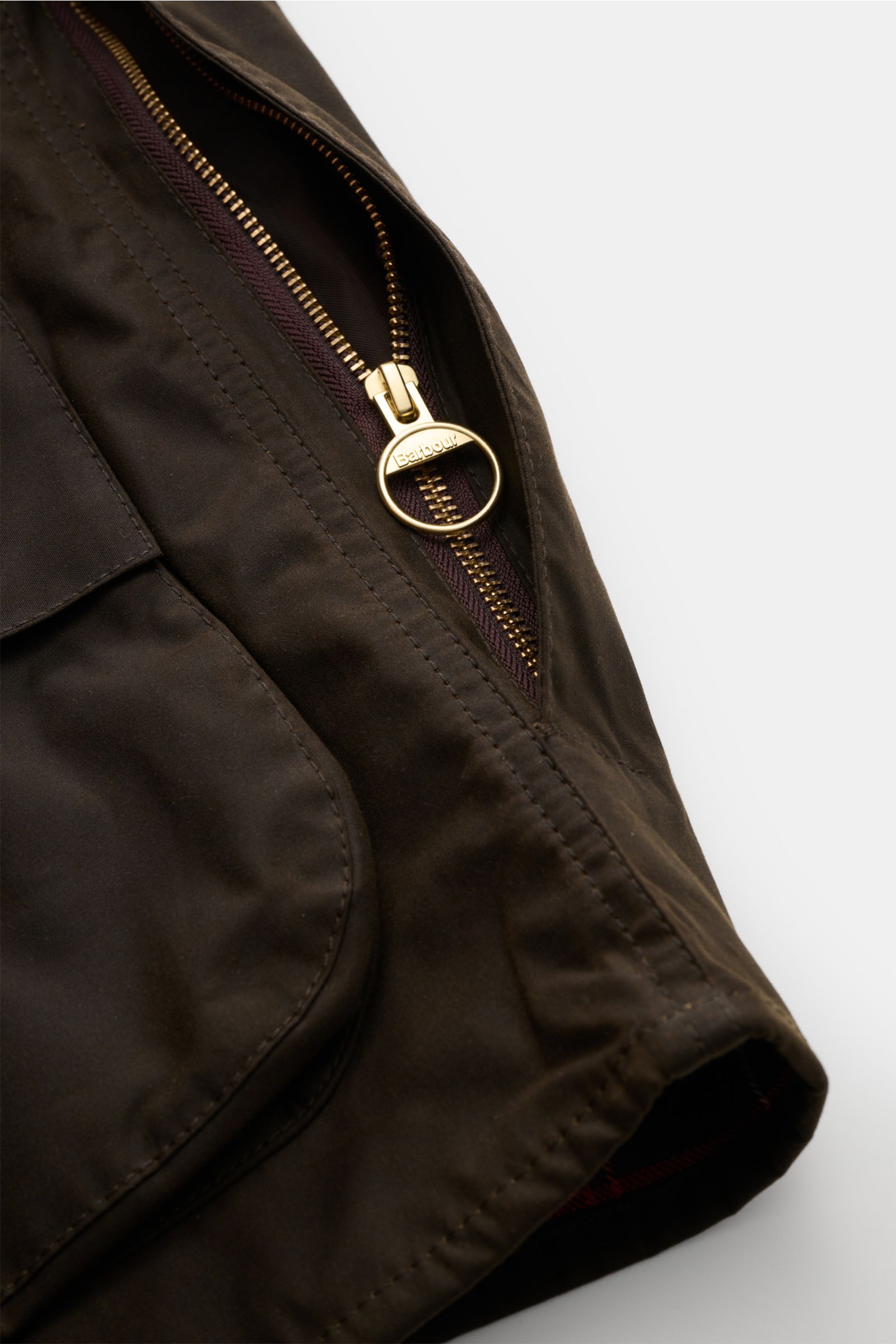 Close-up angled view of the Barbour Waxed jacket 'Beaufort' dark olive showing the waxed cotton fabric, two-way zip with branded pull, and patch pocket.

Description: A true classic from BARBOUR: The long waxed jacket 'Beaufort' made of water repellent, w