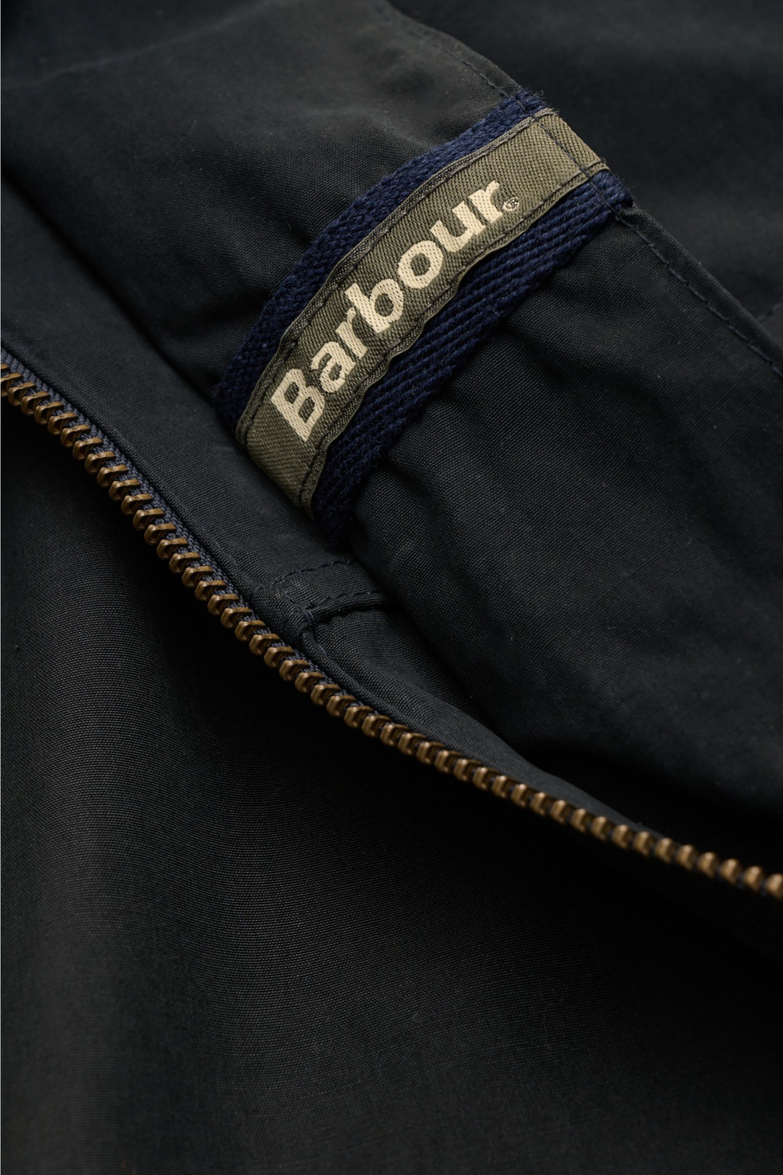 Close-up front view of the Barbour Field jacket 'Sanderling' navy focusing on the zipper and fabric label. Lightweight, functional, classic style with four bellows pockets, cotton-microfibre blend, velvety feel, regular fit, two-way zip, storm flap with s