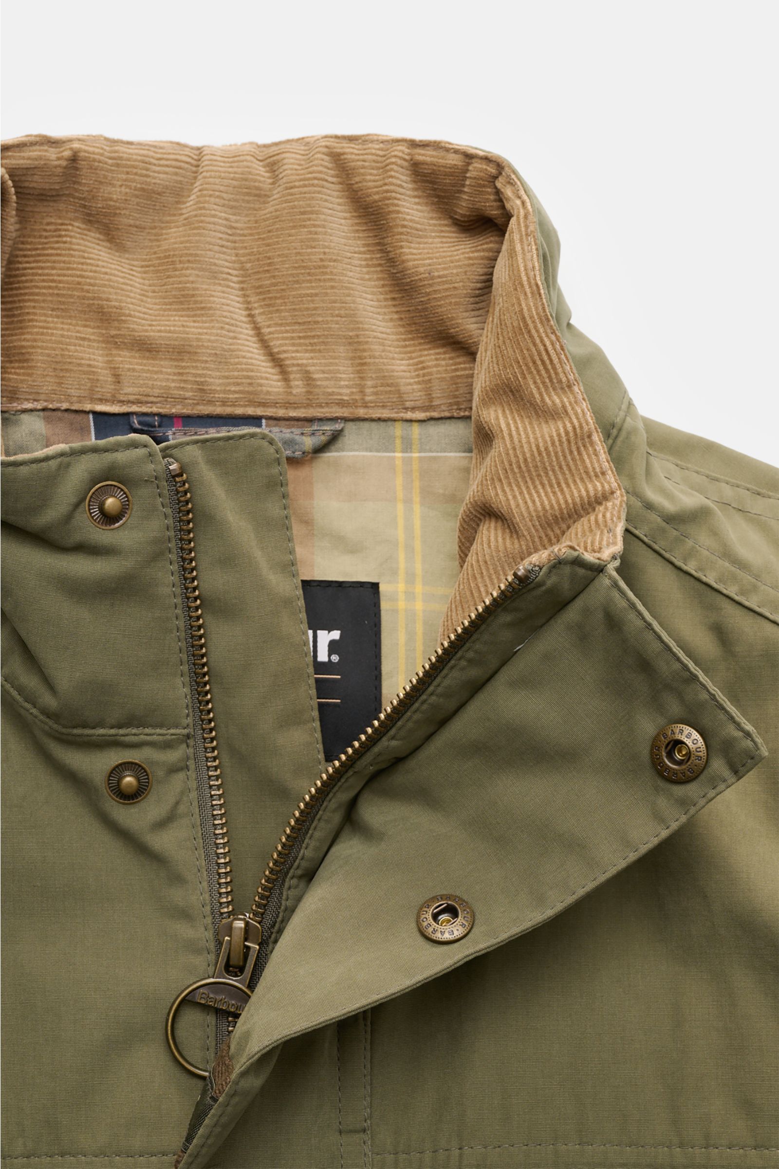Close-up front view of Barbour Field jacket 'Sanderling' olive showing the corduroy-trimmed standing collar, robust two-way zip, storm flap with snap buttons, and part of the tartan-patterned half lining. Lightweight, functional and in classic style: The 