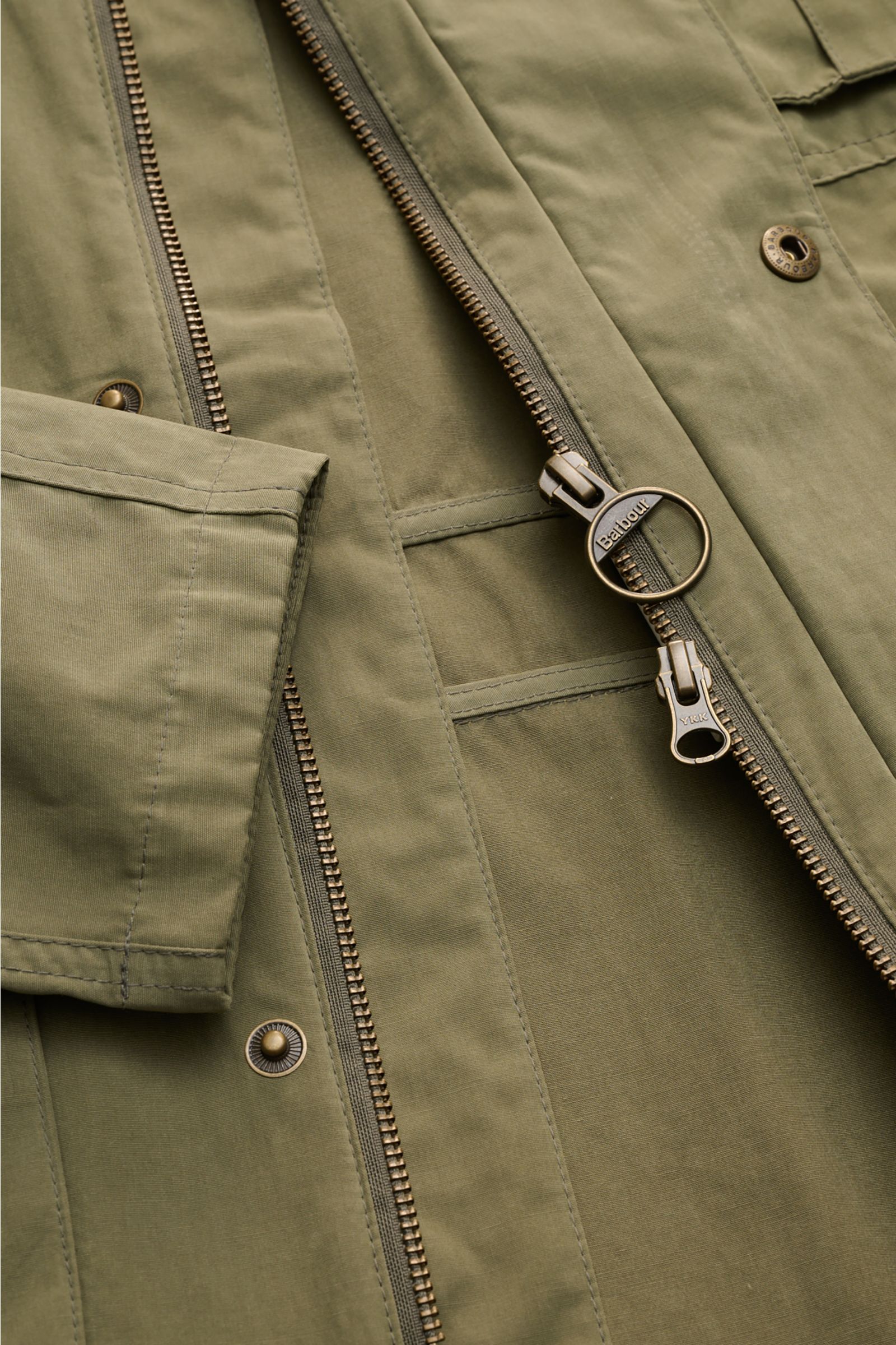 Close-up front view of the Barbour Field jacket 'Sanderling' olive, showing zipper, snap buttons, and fabric texture, lightweight cotton blend.