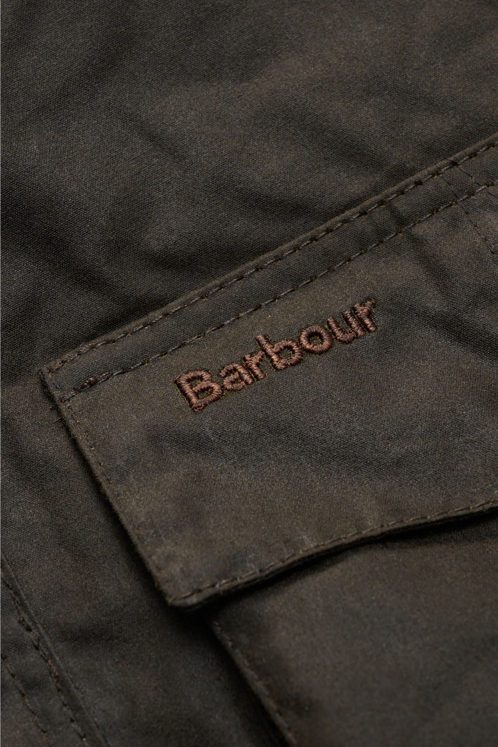 Close-up front view of the Barbour Waxed jacket 'Sander' dark olive showing the waxed cotton pocket flap with embroidered Barbour logo, highlighting the pure waxed cotton, water repellent fabric, regular fit, robust two-way zip, storm flap with snap butto