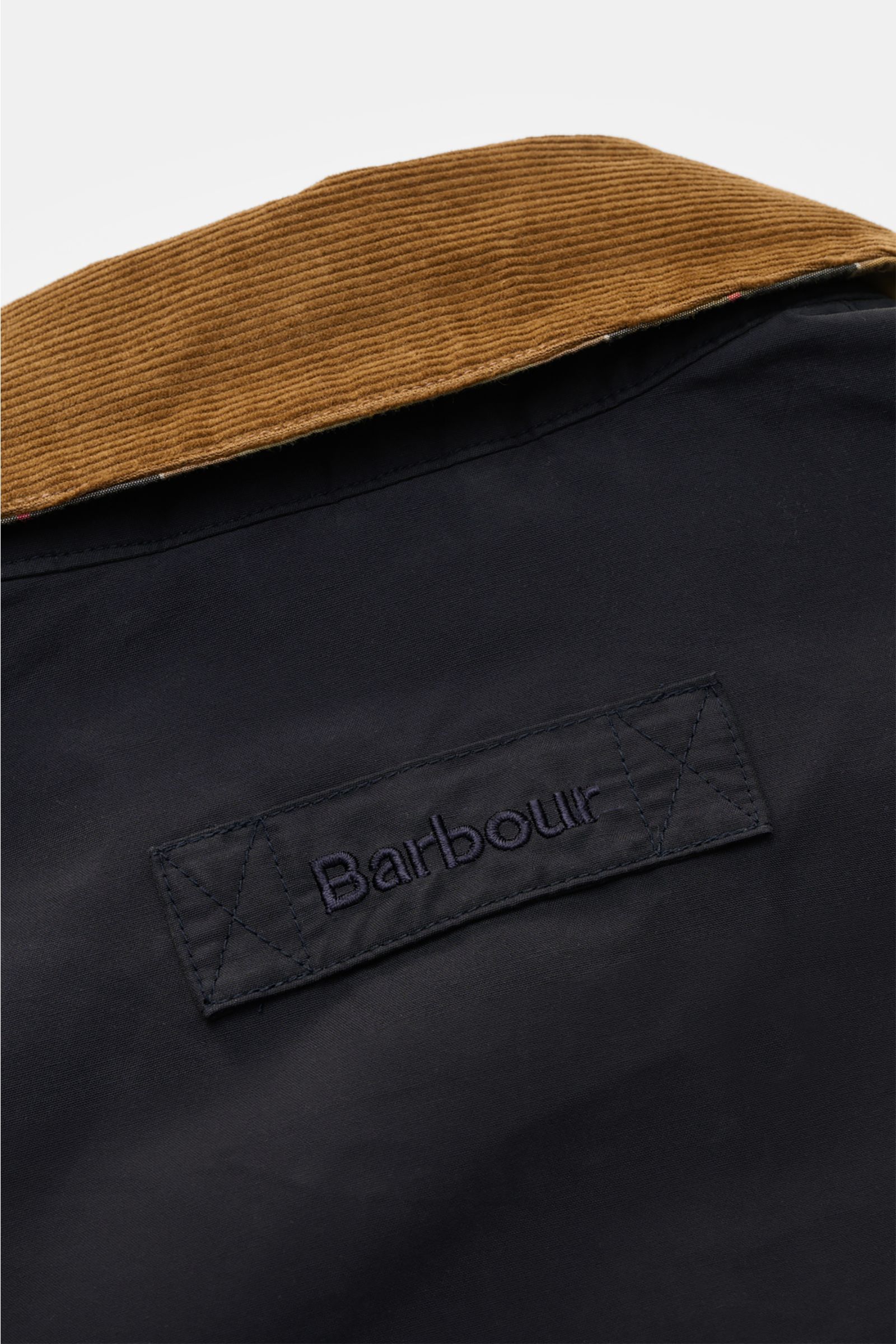 Close-up from above of the Barbour Parka 'Icons Border' dark navy showing the brown corduroy turn-down collar and embroidered logo on the back.

Description:
Create classically elegant casual looks in quintessentially English style with the lightweight