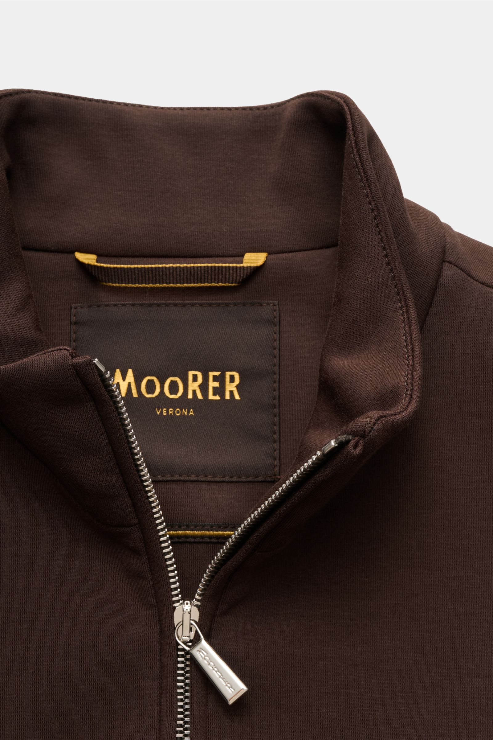 Nahaufnahme der Moorer Sweatjacke 'Crispin Felpa' dunkelbraun von oben, zeigt Stehkragen, Zipper-Fronttaschen, zwei-Wege-Reißverschluss, Slim Fit aus Baumwoll-Mischung.