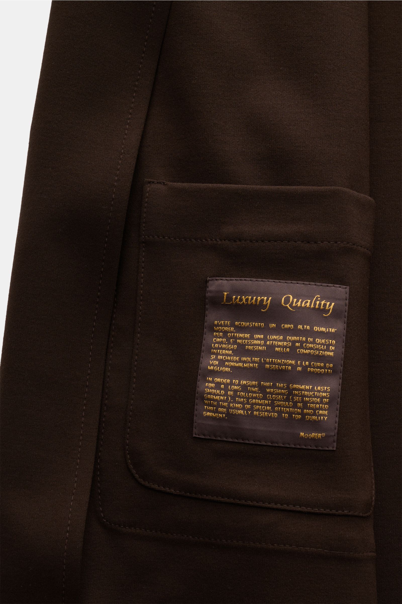 Close-up front view of the dunkelbraun Moorer Jersey-Jacke 'Keaton' showing the patch pocket with a luxury quality label. So fühlt sich Luxus an: Die leichte Jacke 'Keaton' von MOORER im Overshirt-Stil kombiniert edlen Materialmix mit geradlinigem Schn