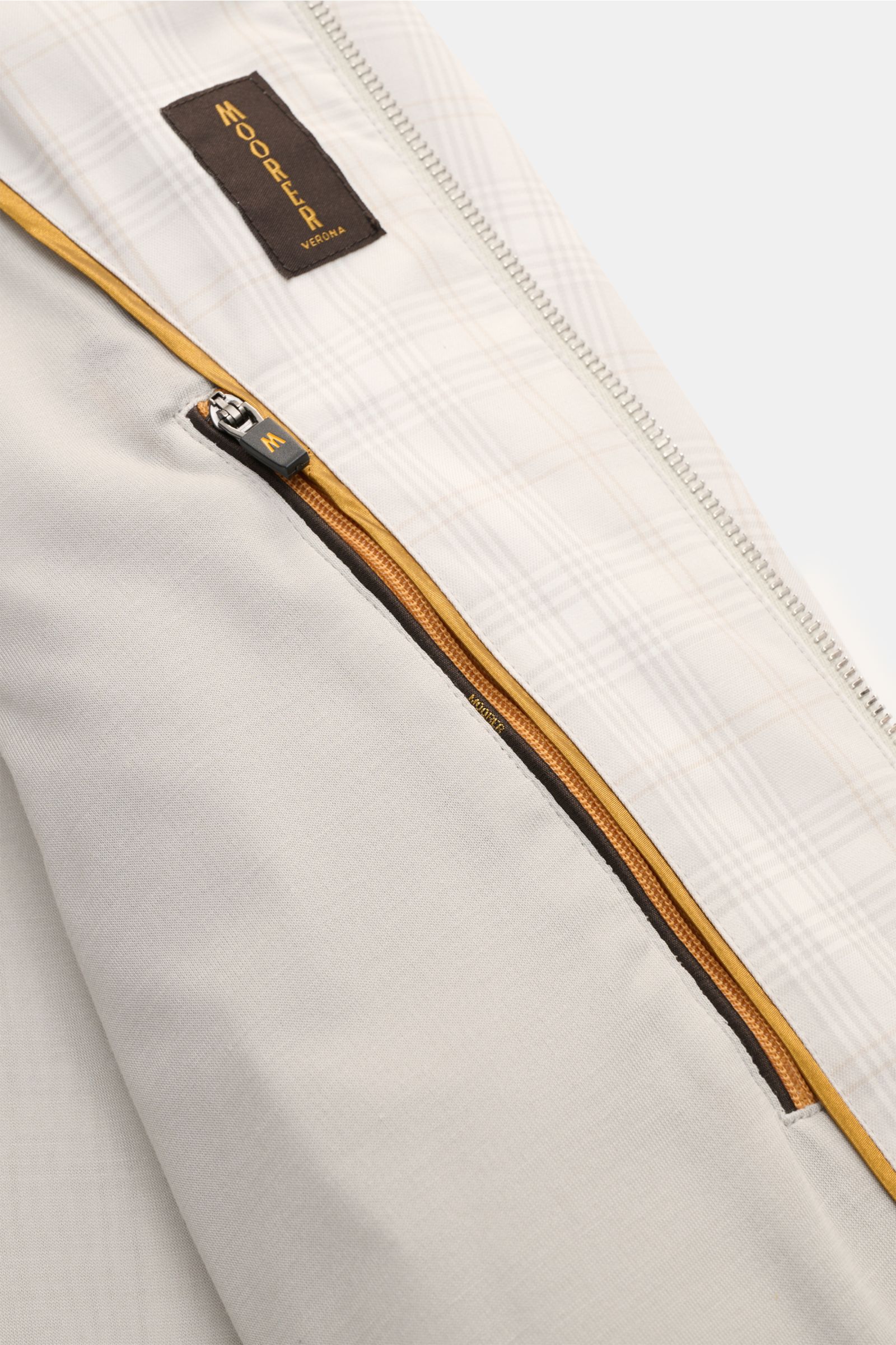 Close-up interior view of the Moorer Blouson 'Sorano' light grey/beige/cream checked, showing the soft jersey lining, zip front pocket with mustard yellow trim, two-way silver zipper, and MOORER Verona label on the classic checked pattern fabric. The luxu