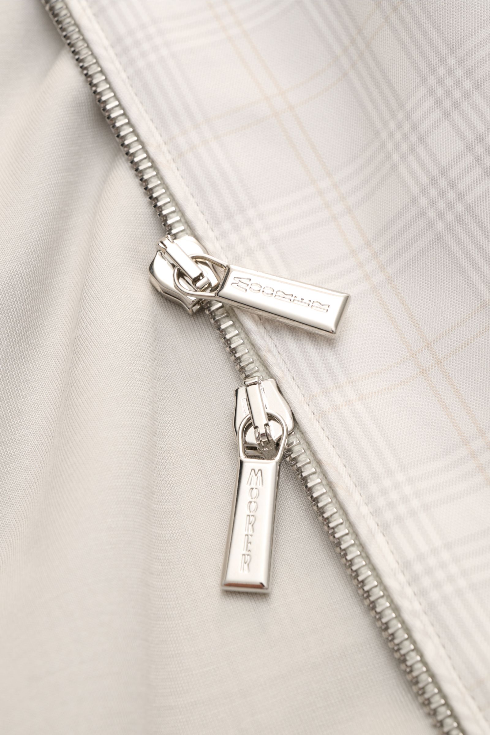 Close-up front view of the silver two-way zip with 'MOORER' engraving on the Moorer Blouson 'Sorano' light grey/beige/cream checked, made of pure cotton with a classic checked pattern and soft feel.