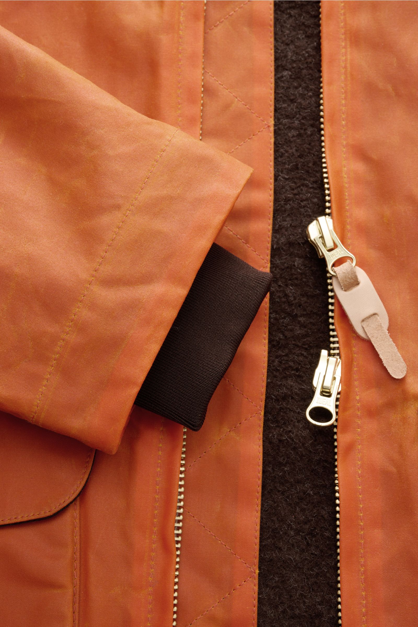 Nahaufnahme der Manifattura Ceccarelli Wachsjacke 'Blazer Coat' orange von vorne, zeigt gewachste Baumwolle, Lederdetails, Zwei-Wege-Reißverschluss, Stehkragen mit Alpakawolle und elastisches Windschutzbündchen.
