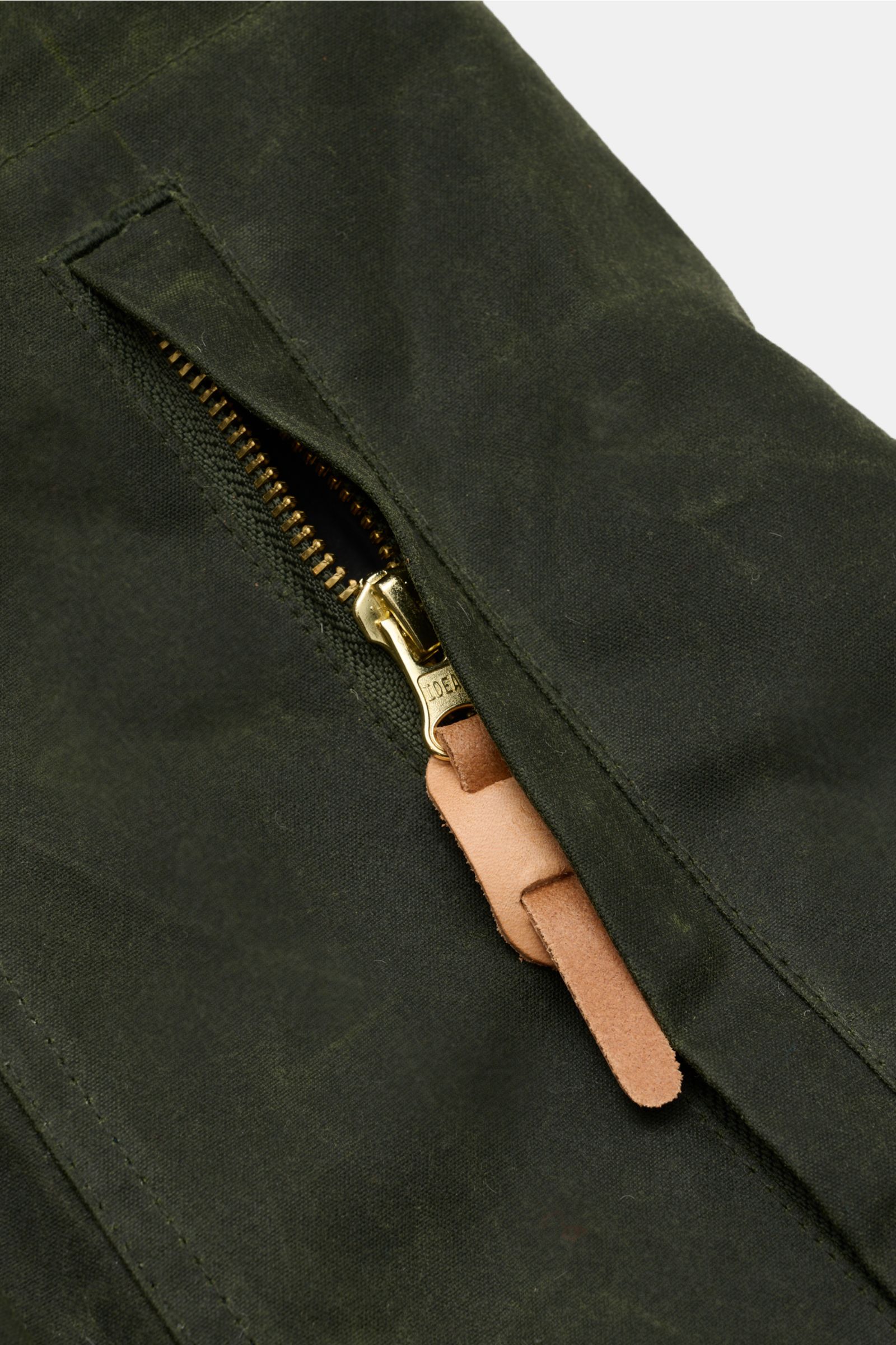 Nahaufnahme des Reißverschlusses mit Lederlasche der Manifattura Ceccarelli Wachsjacke 'New Fisherman' oliv aus gewachster Baumwolle.