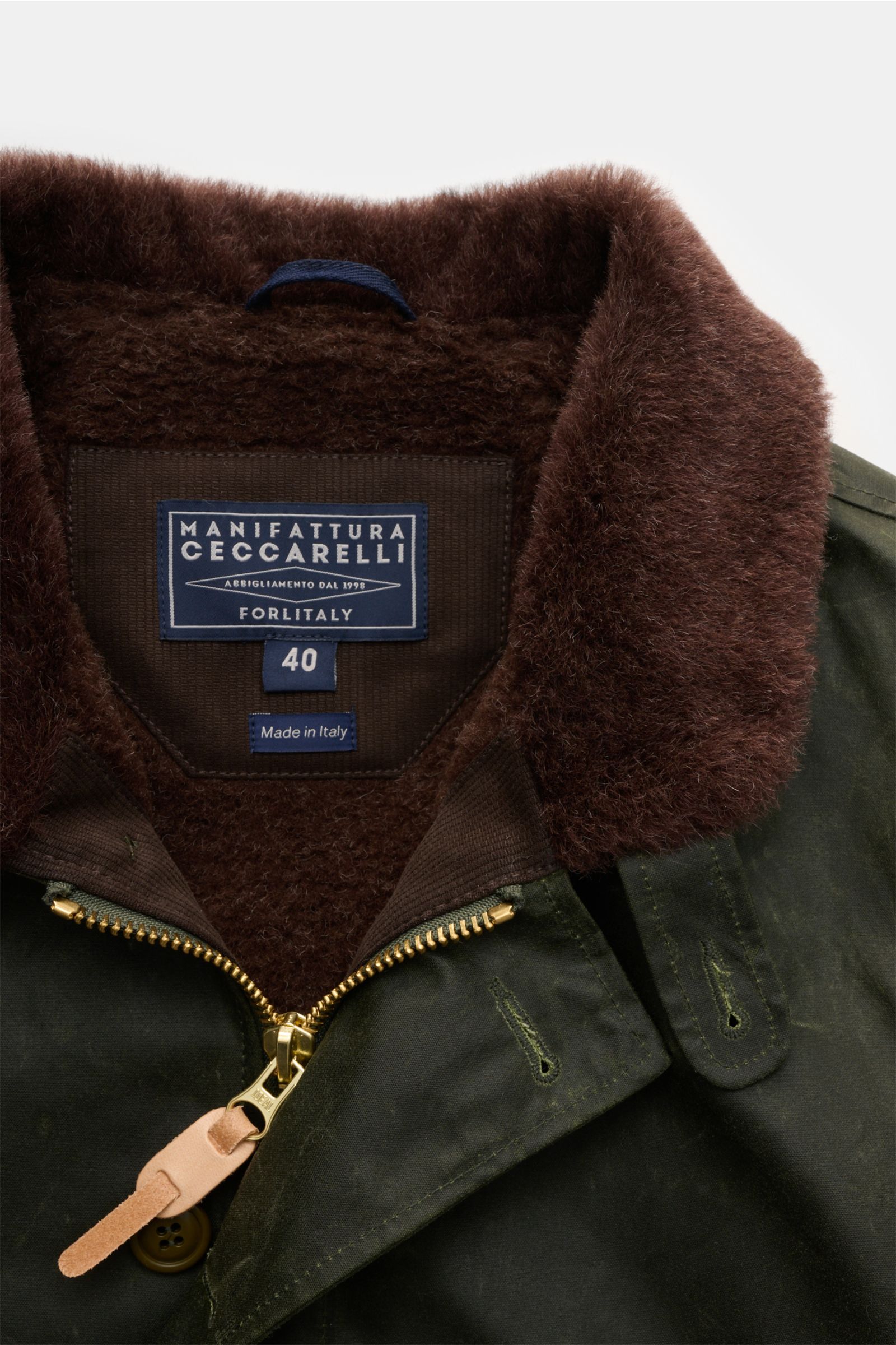 Nahaufnahme von Kragen und Reißverschluss der Manifattura Ceccarelli Wachsjacke 'Deck Jacket' dunkelgrün, mit braunem Alpakawollfutter, robustem Zwei-Wege-Reißverschluss und verstellbarem Tunnelzug, fotografiert von vorn oben.