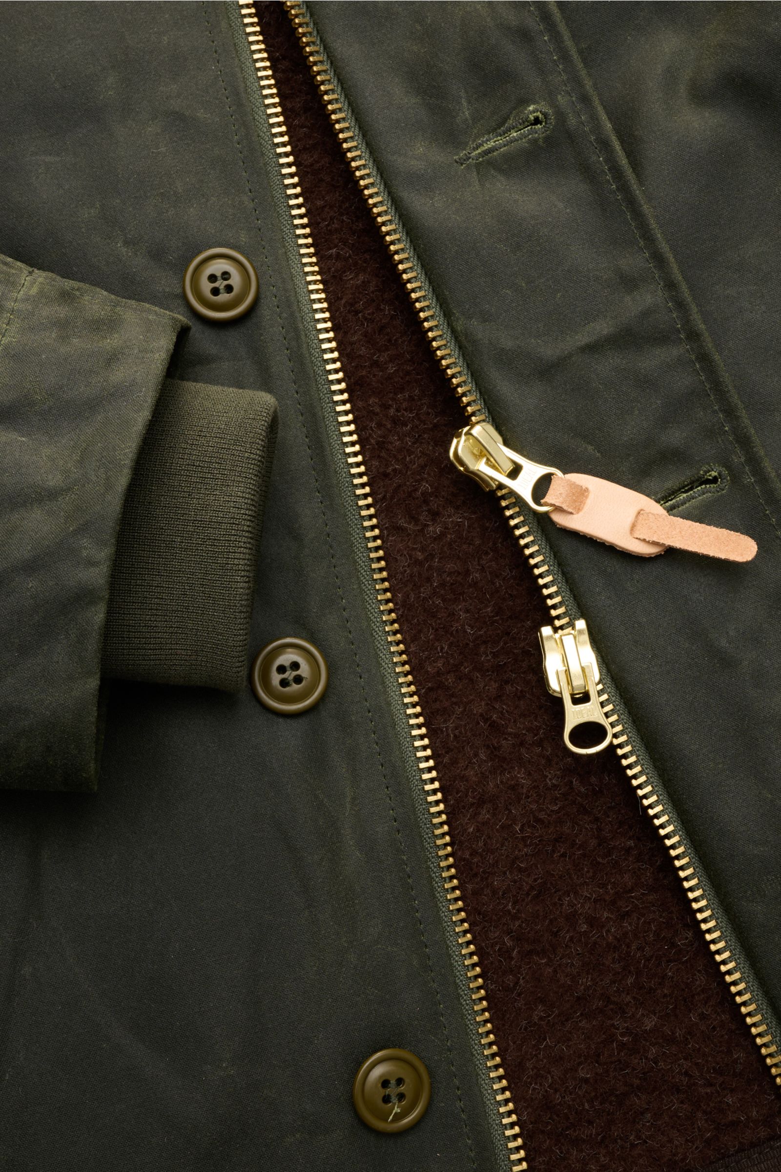 Manifattura Ceccarelli Wachsjacke 'Deck Jacket' dunkelgrün, Detailaufnahme von Reißverschluss, Knöpfen, gewachster Baumwolle und Wollfutter.