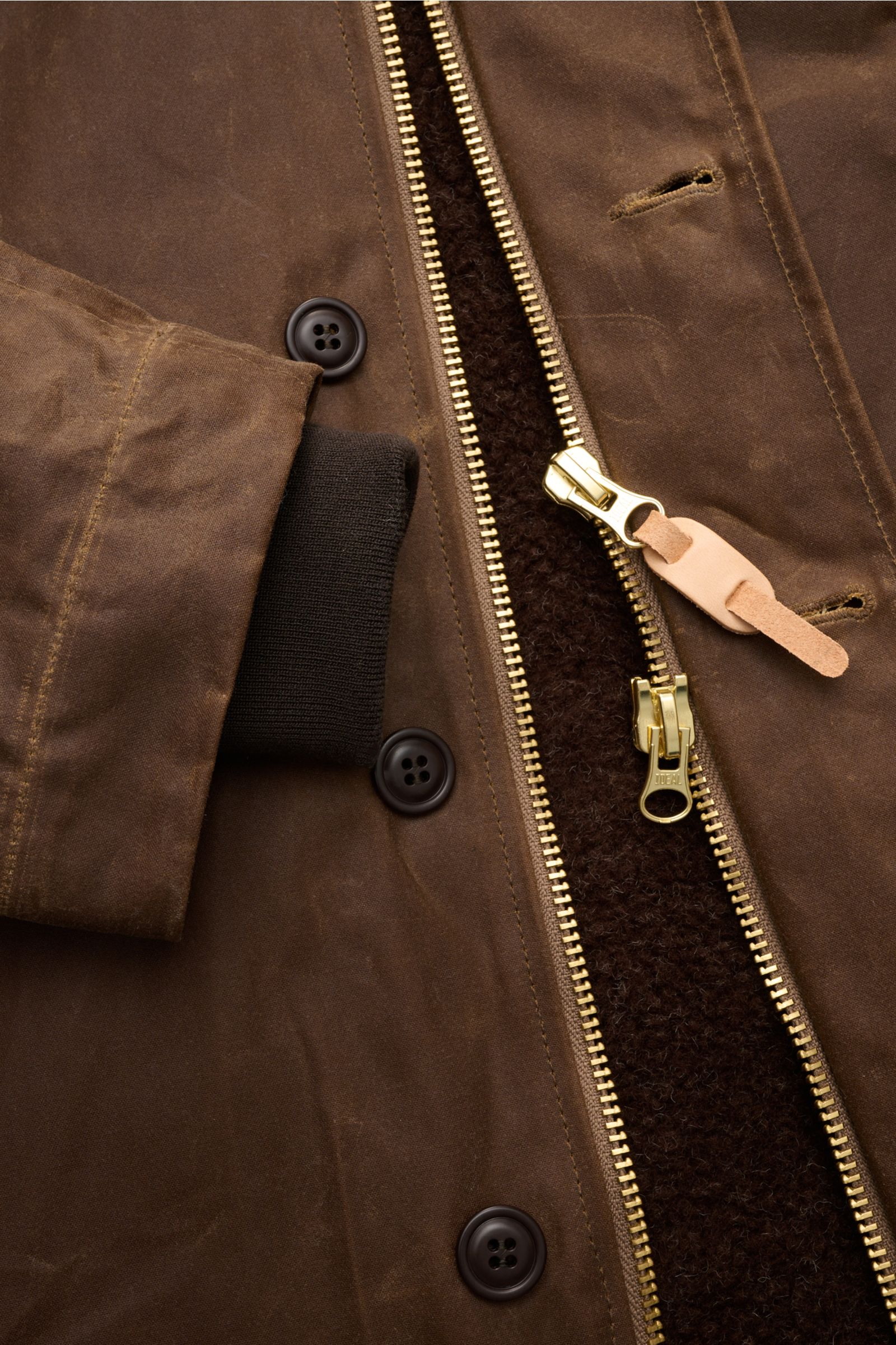 Nahaufnahme der Manifattura Ceccarelli Wachsjacke 'Deck Jacket' braun von oben, zeigt gewachste Baumwolle, robusten Zwei-Wege-Reißverschluss mit Lederlasche, Knöpfe, elastisches Bündchen und warmes Alpakawollfutter.