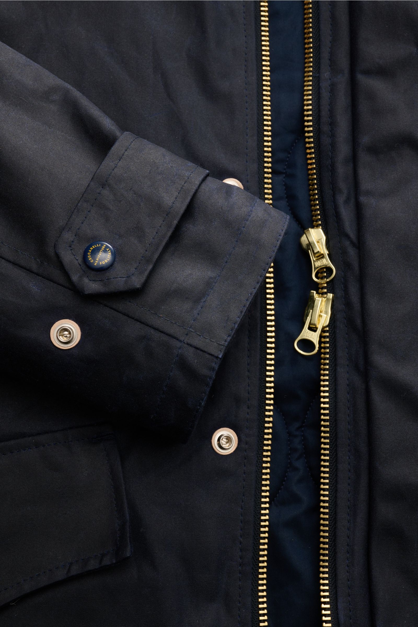 Nahaufnahme des Manifattura Ceccarelli Wachsparka 'Mountain' navy von schräg oben, zeigt Reißverschluss, Druckknöpfe und Ärmel mit Logo.
