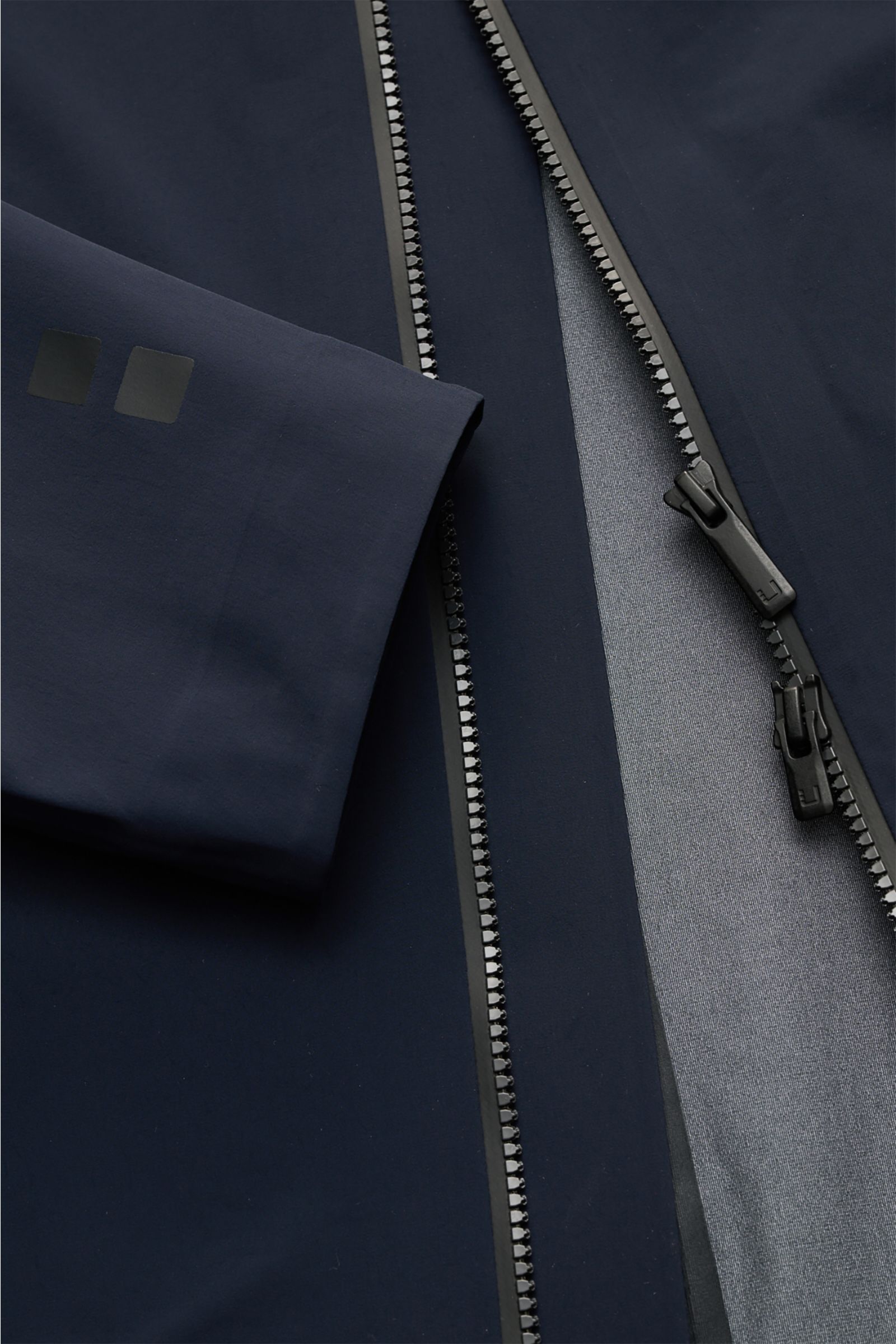UBR Kurzmantel 'Delta' navy in Nahaufnahme von oben, zeigt glatten Stoff, zwei-Wege-Reißverschluss, Ärmel mit Logo, elastische Microfaser.