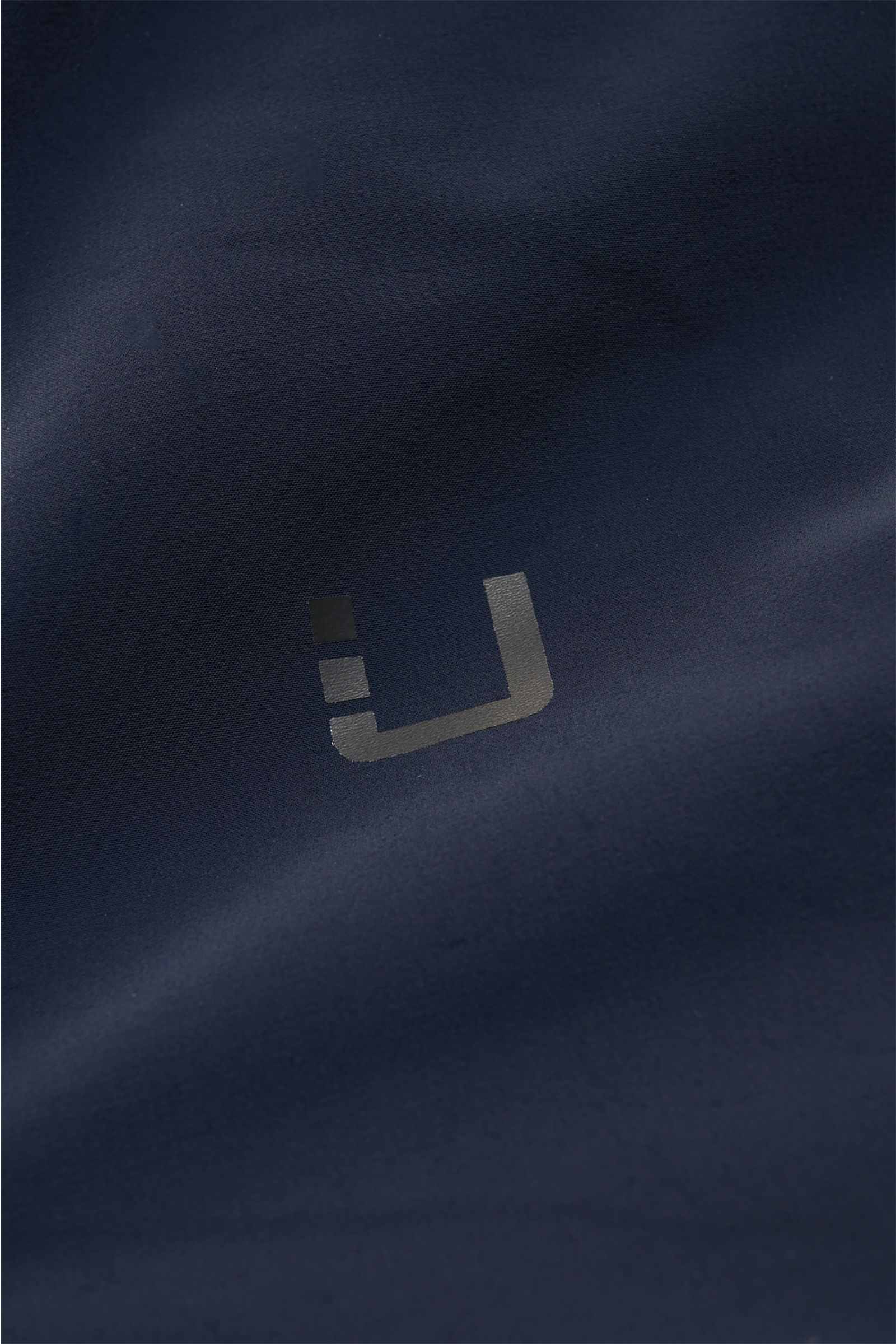 UBR Kurzmantel 'Delta' navy Detailaufnahme der glatten, elastischen Microfaser-Oberfläche mit reflektierendem Logo, frontale Perspektive.