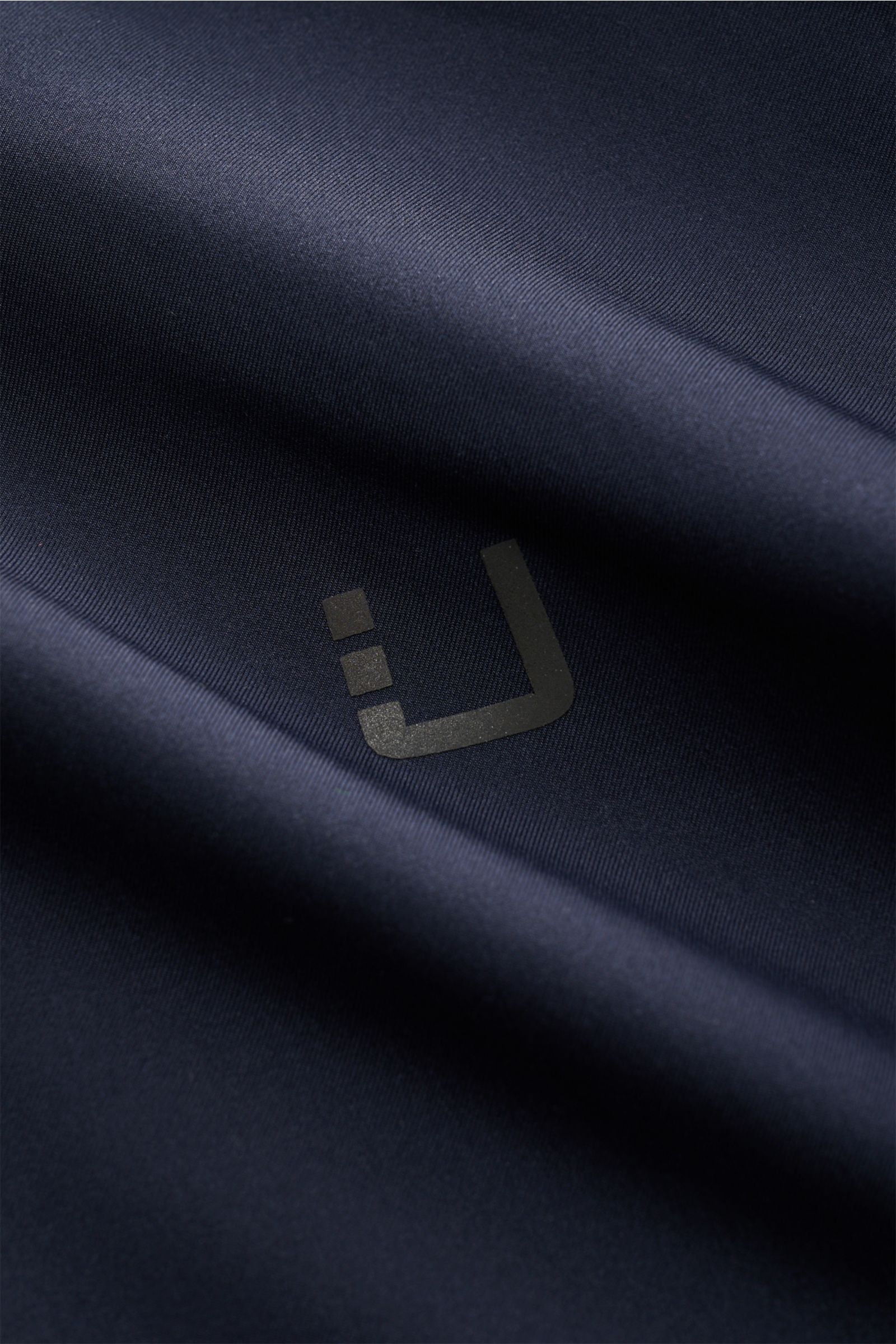 UBR Jacke 'Nano' navy Nahaufnahme glatter Microfaser mit reflektierendem Logo, wind- und wasserabweisend, aus Frontperspektive.
