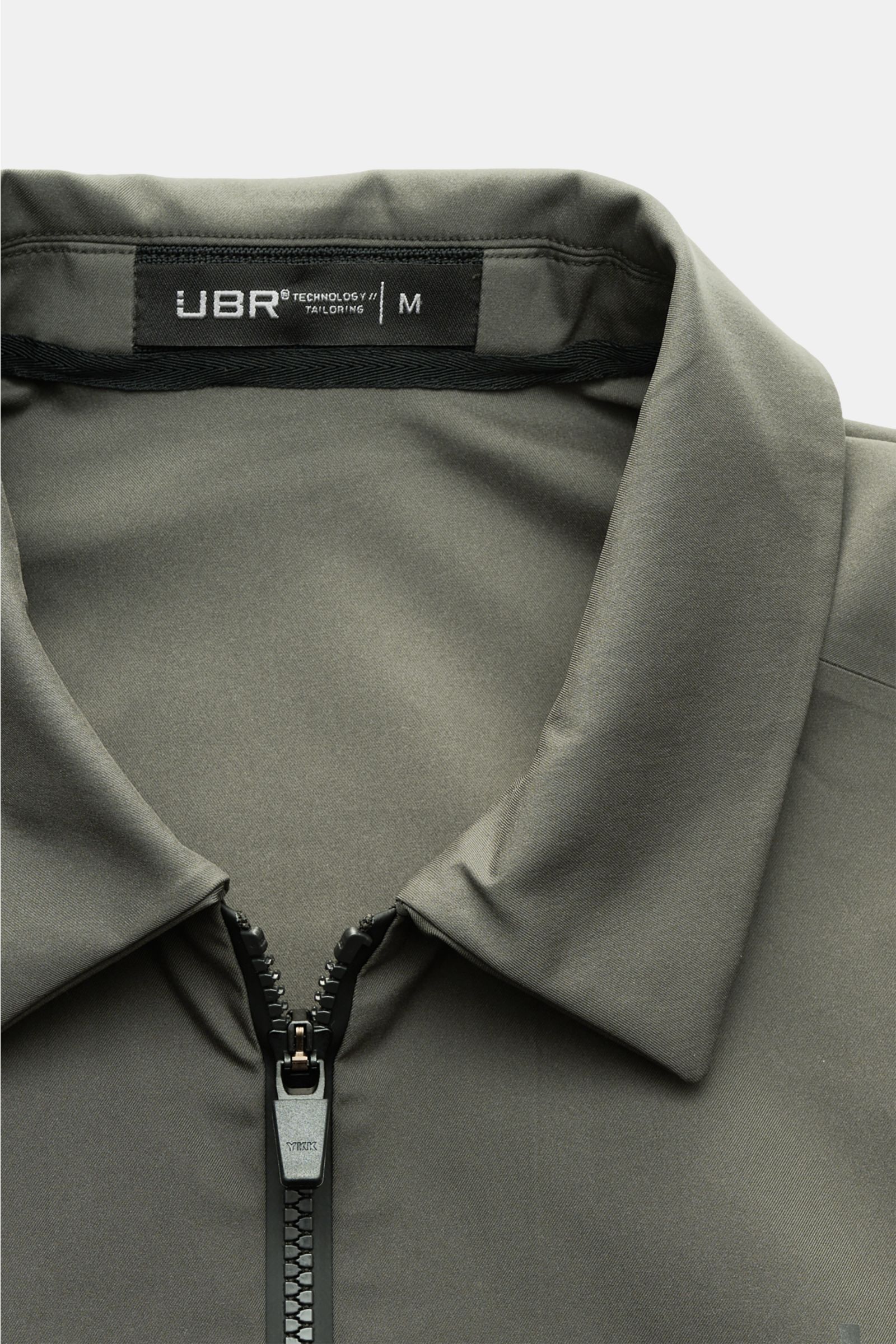 Nahaufnahme der UBR Jacke 'Nano' graugrün von oben frontal, zeigt glatten Microfaserstoff, Umlegekragen und zwei-Wege-Reißverschluss, wind- und wasserabweisend, slim fit, elastische Ärmelabschlüsse, reflektierender Logo-Print.