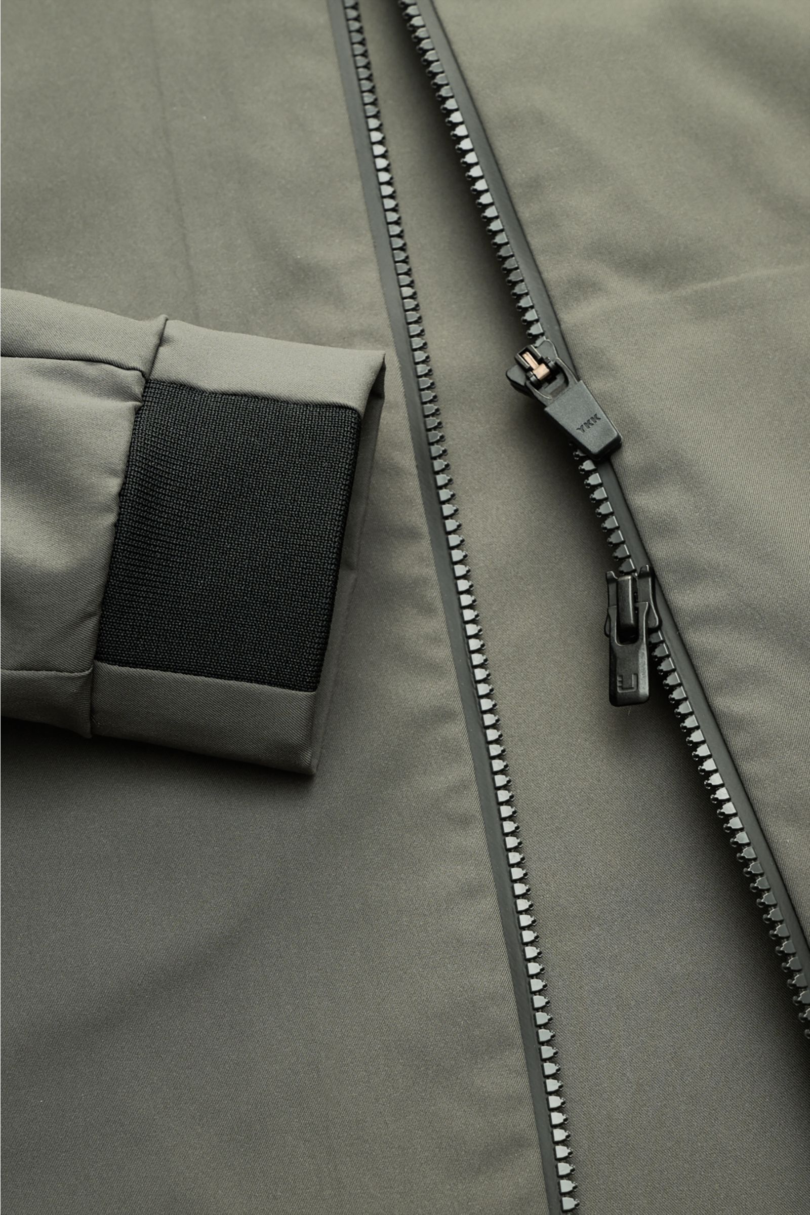 UBR Jacke 'Nano' graugrün in Nahaufnahme von vorne, zeigt glatten Microfaserstoff, Zwei-Wege-Reißverschluss und flexible Ärmelabschlüsse.