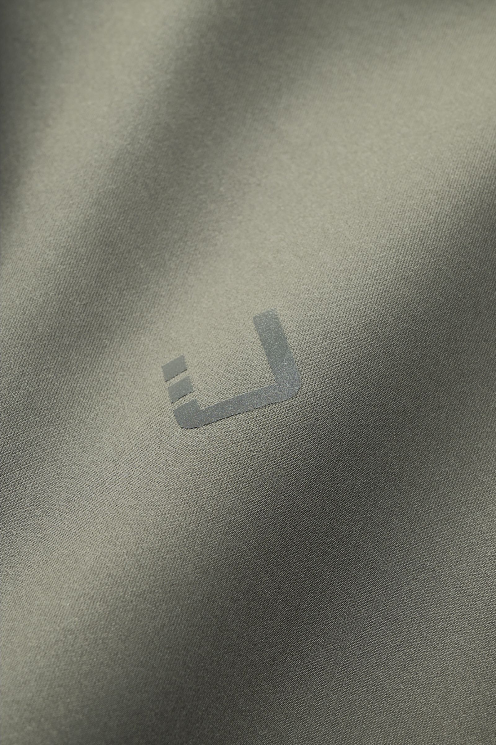 UBR Jacke 'Nano' graugrün im Detail, Stoffnahaufnahme mit reflektierendem Logo-Print, glatter Griff, wind- und wasserabweisend, Slim Fit.