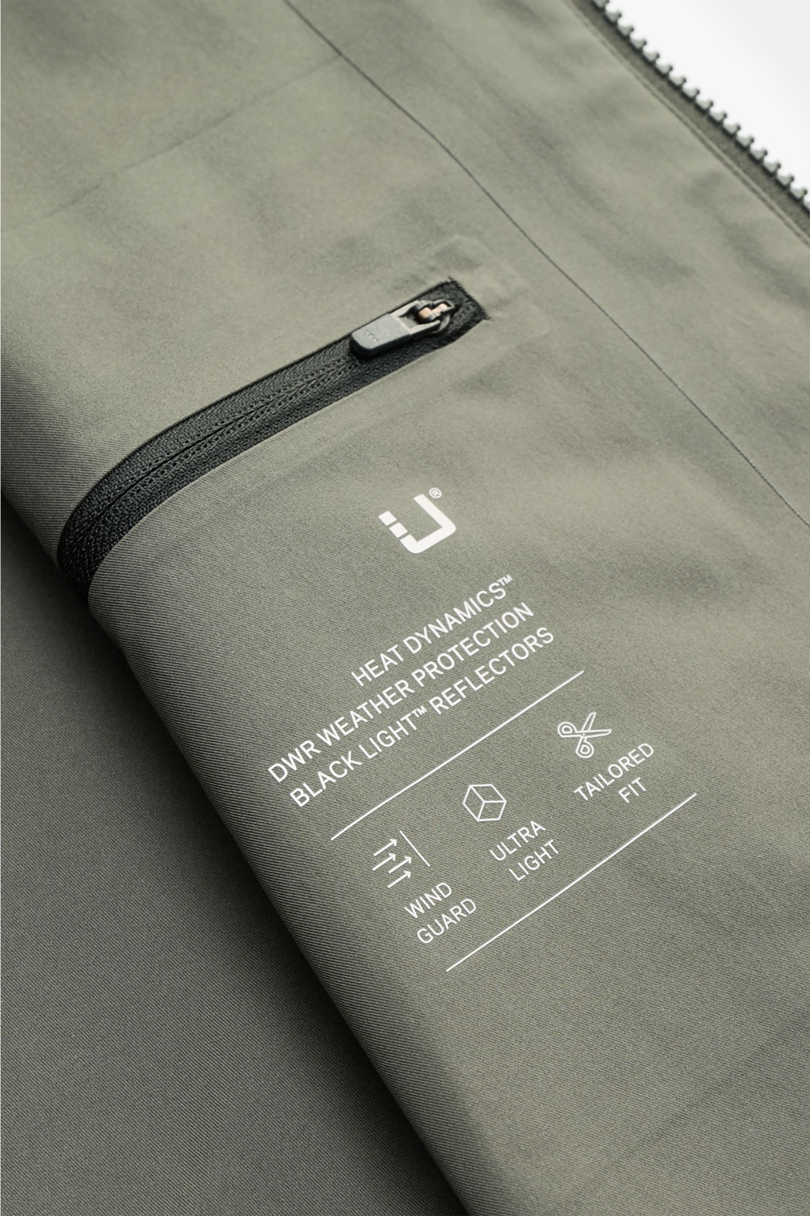UBR Jacke 'Nano' graugrün aus leichter Microfaser, wind- und wasserabweisend, mit Reißverschluss und reflektierendem Logo, Detail nah fotografiert.