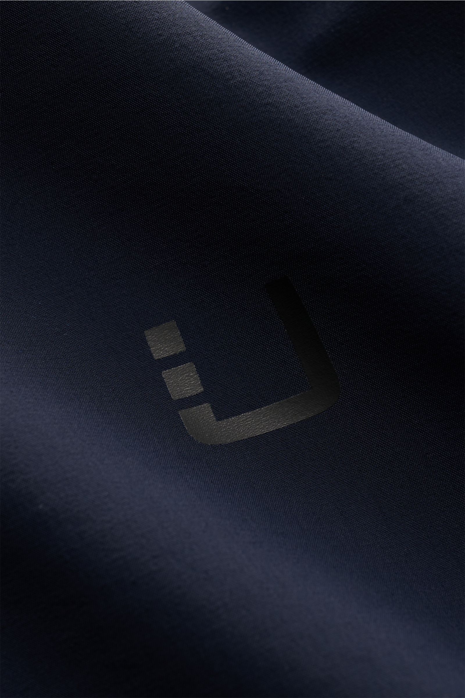 UBR Blouson 'Delta' navy aus hochwertiger Microfaser, Detailaufnahme des glatten Stoffes mit Logo, schräg fotografiert.