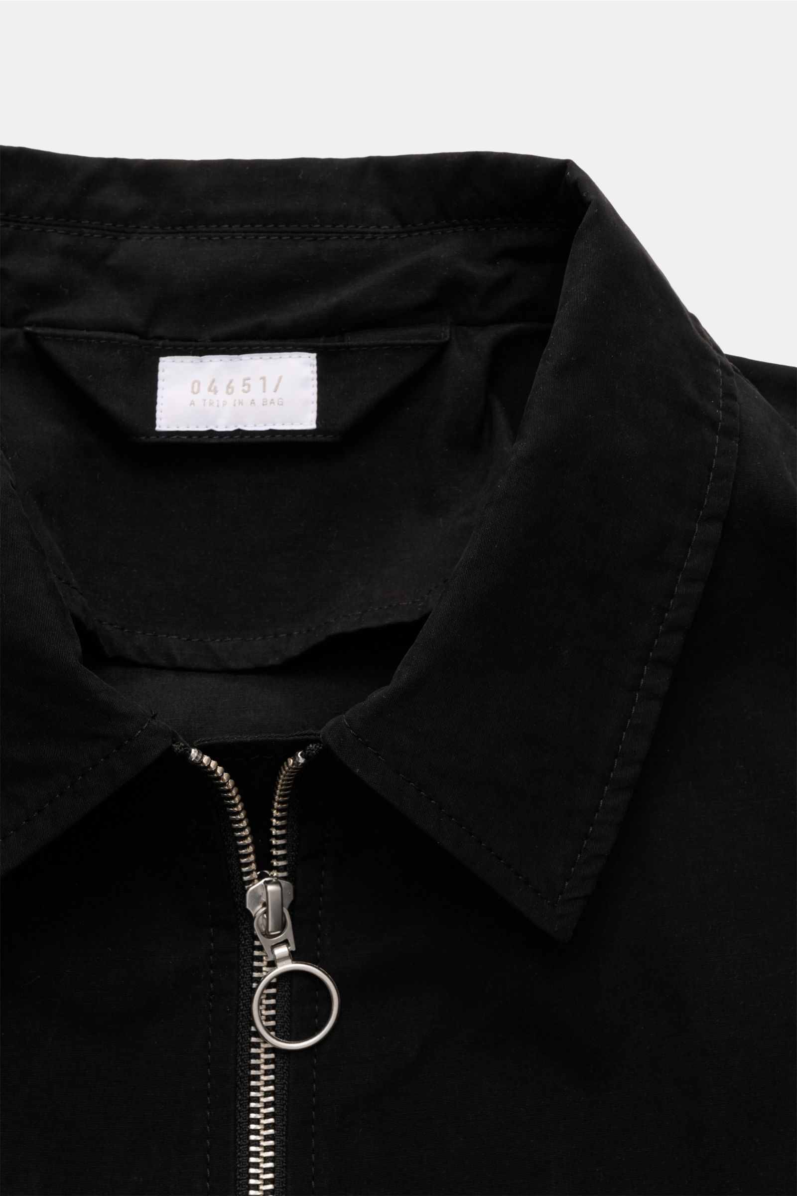 Nahaufnahme des schwarzen 04651/ A trip in a bag Blouson 'Peached Cotton' mit Umlegekragen, robustem Reißverschluss und weichem Material, von oben fotografiert.