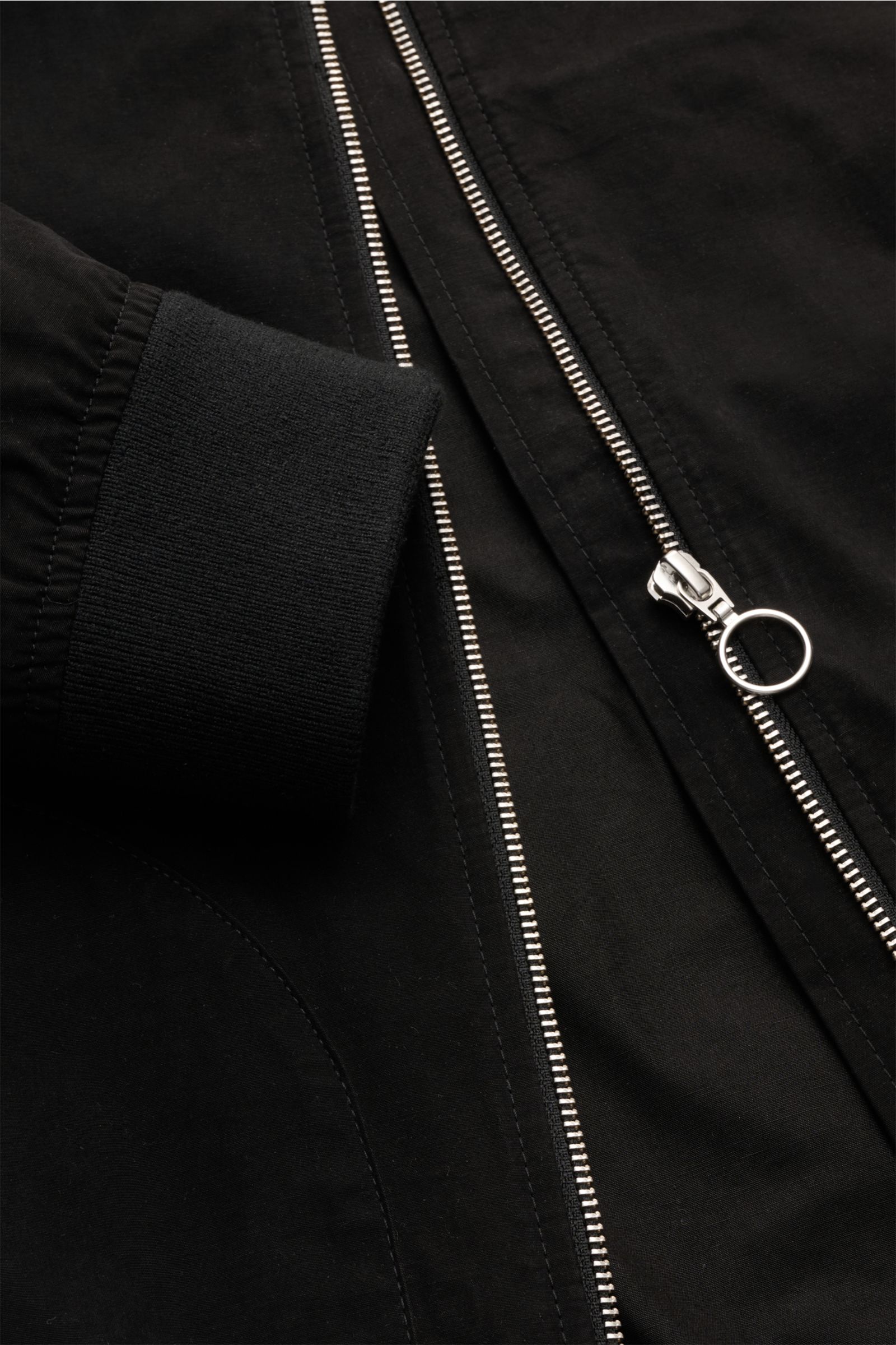 Nahaufnahme aus schräger Perspektive des schwarzen 04651/ A trip in a bag Blouson 'Peached Cotton' mit robustem Reißverschluss, elastischem Ärmelbündchen und softem Baumwoll-Microfaser-Mix.