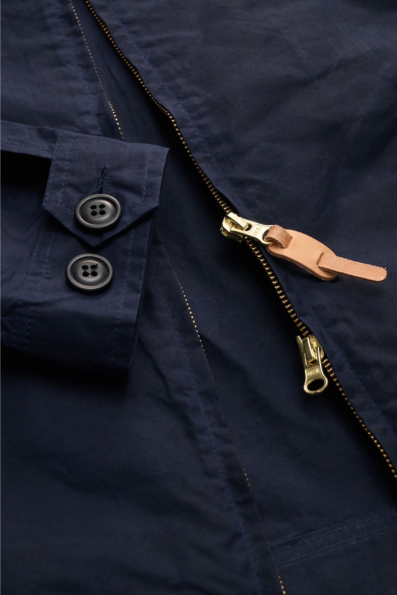 Close-up front view of Manifattura Ceccarelli Waxed jacket 'Blazer Coat' navy showing its navy waxed cotton fabric, robust two-way gold zipper with leather pull, and buttoned cuff details. Authentic outerwear with vintage character: This Italian-made wax 