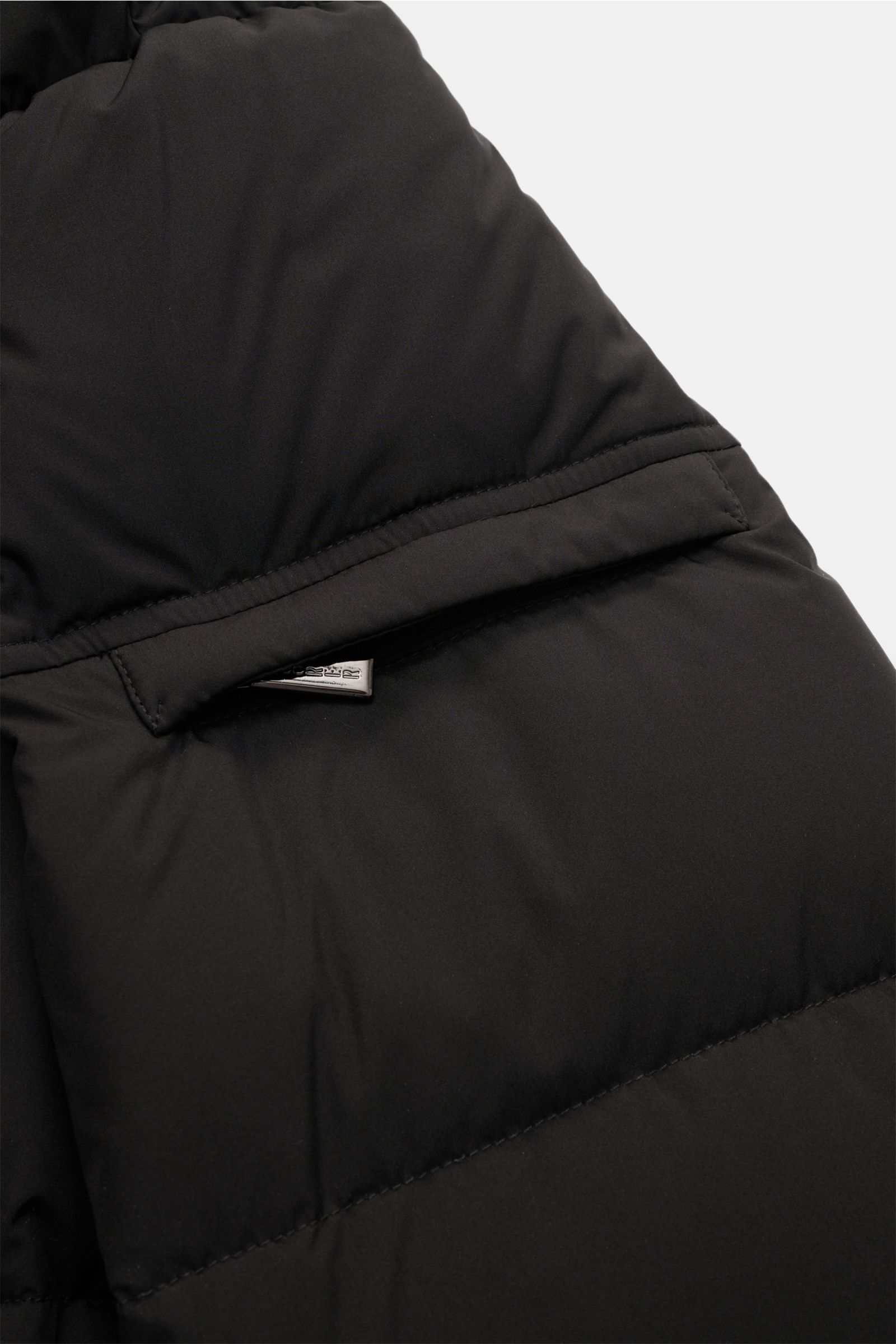 Nahaufnahme der schwarzen Moorer Daunenjacke 'Brett' mit wasserabweisendem Material, abnehmbarer Kapuze und Reißverschluss, aus schräger Perspektive.