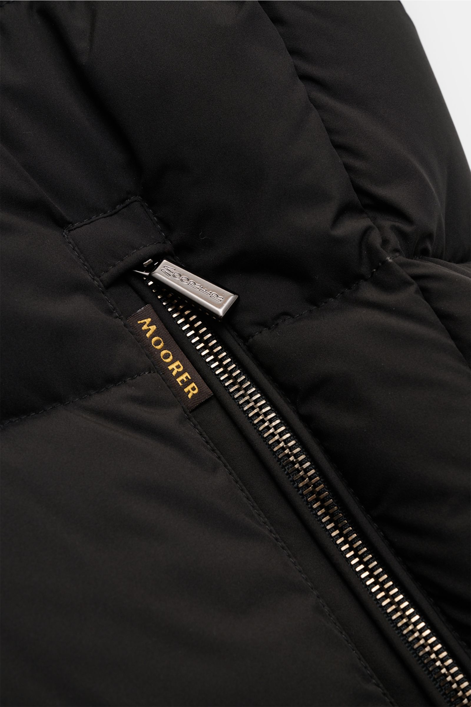 Nahaufnahme der schwarzen Moorer Daunenjacke 'Brett' mit wasserabweisendem Material, Reißverschluss und Markenlabel.