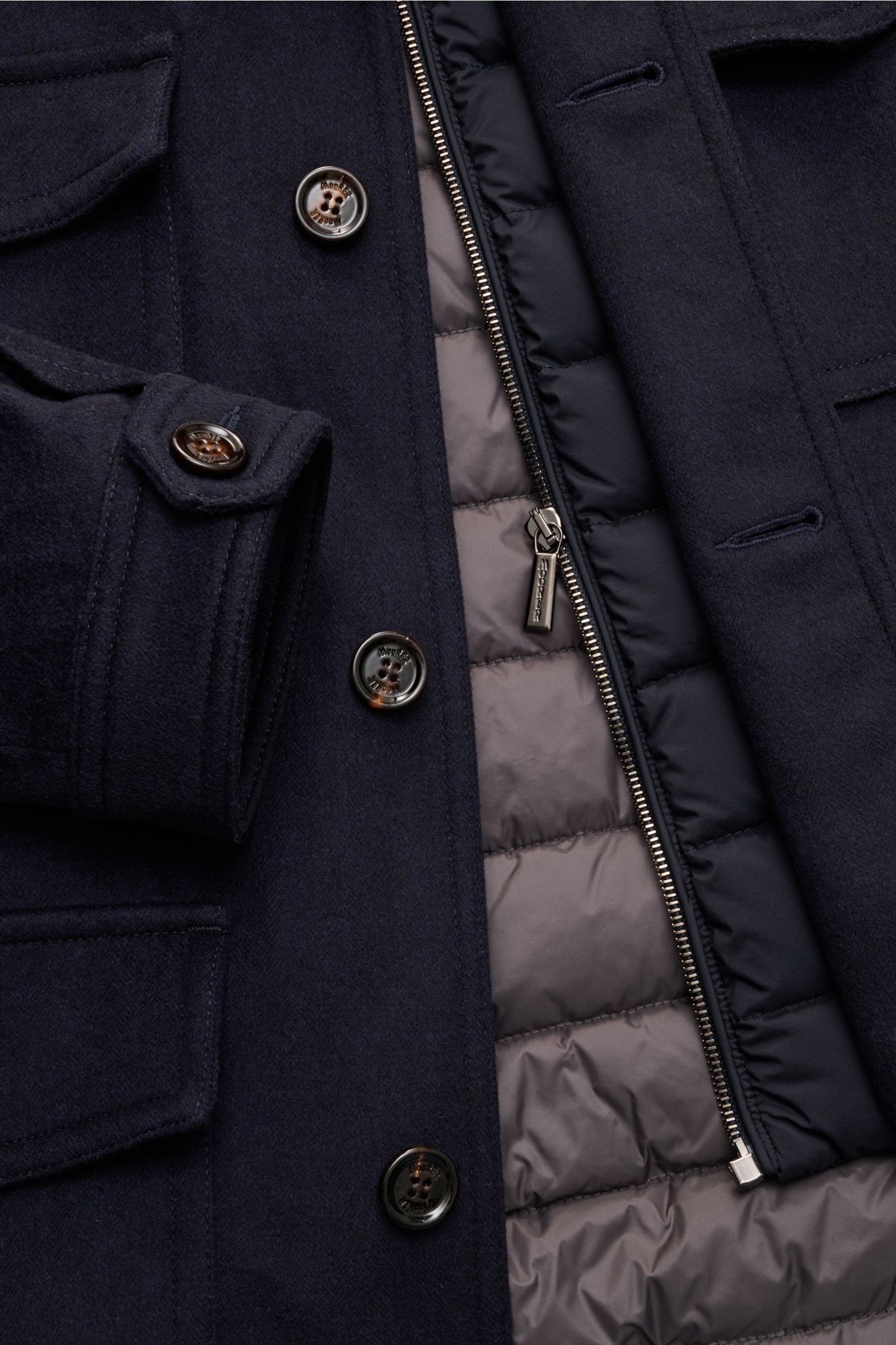 Nahaufnahme der Moorer Daunenjacke 'Monti' navy von vorne, zeigt Wolle-Cashmere-Mix, fünf Knöpfe, Reißverschluss der herausnehmbaren Double-Front mit Kapuze, vier Fronttaschen und gesteppte Daunenfüllung.
