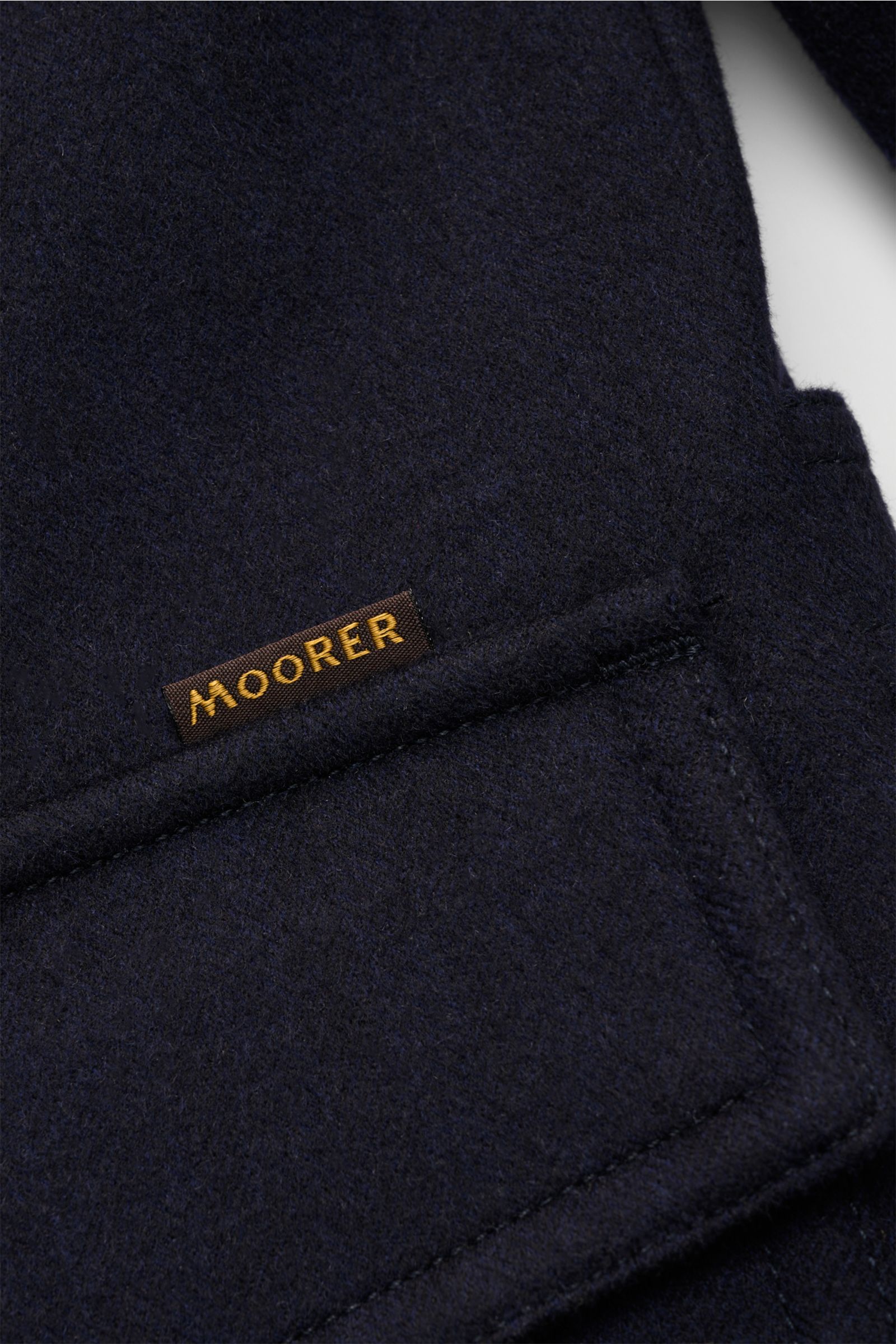 Moorer Daunenjacke 'Monti' navy Detailfoto der wasserabweisenden Woll-Cashmere-Mischung mit Label auf der Fronttasche, Slim Fit.