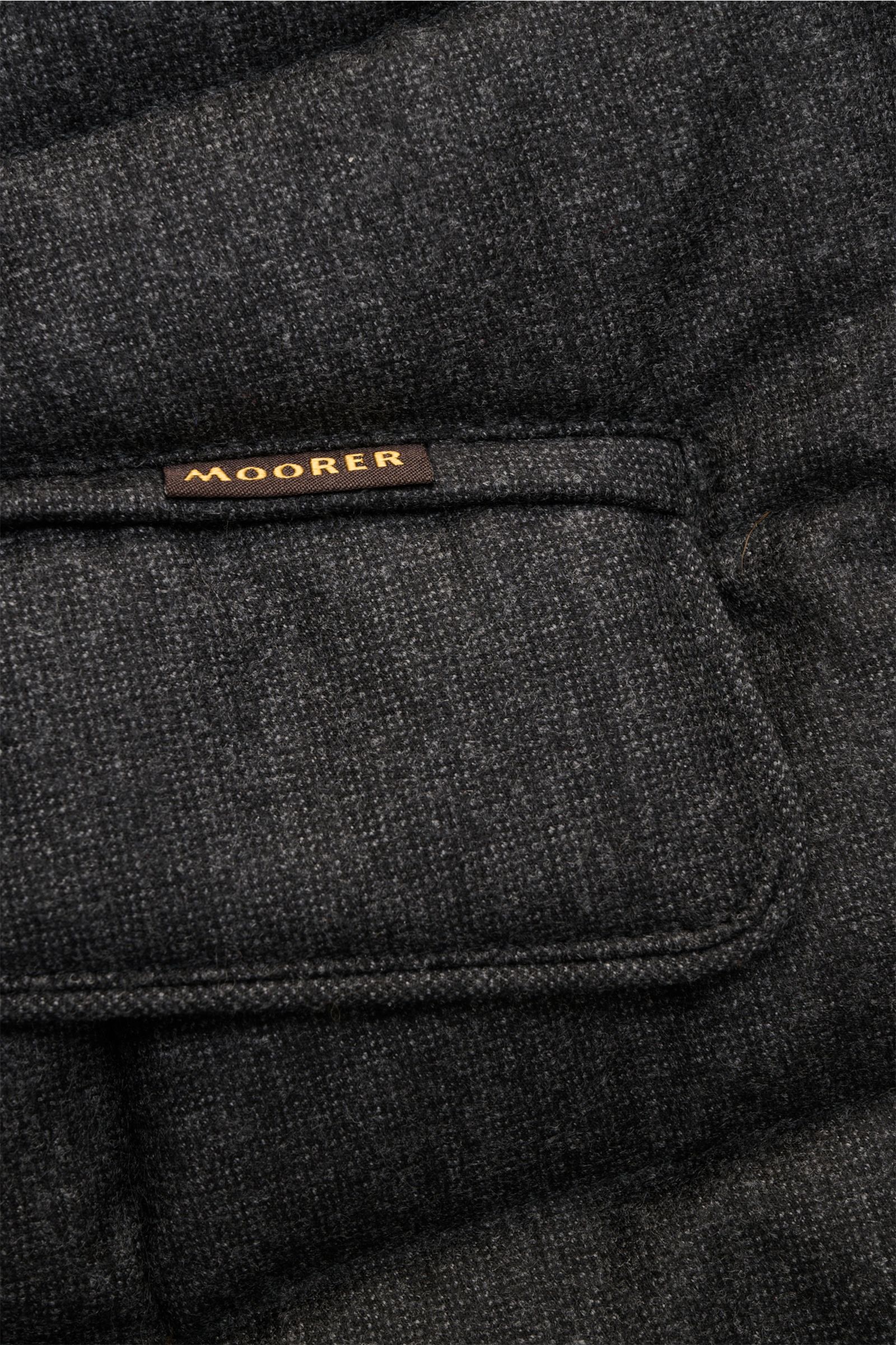 Nahaufnahme der Taschenklappe mit kleinem Moorer-Label der dunkelgrau melierten Moorer Daunenjacke 'Nomos' aus reiner Wolle.