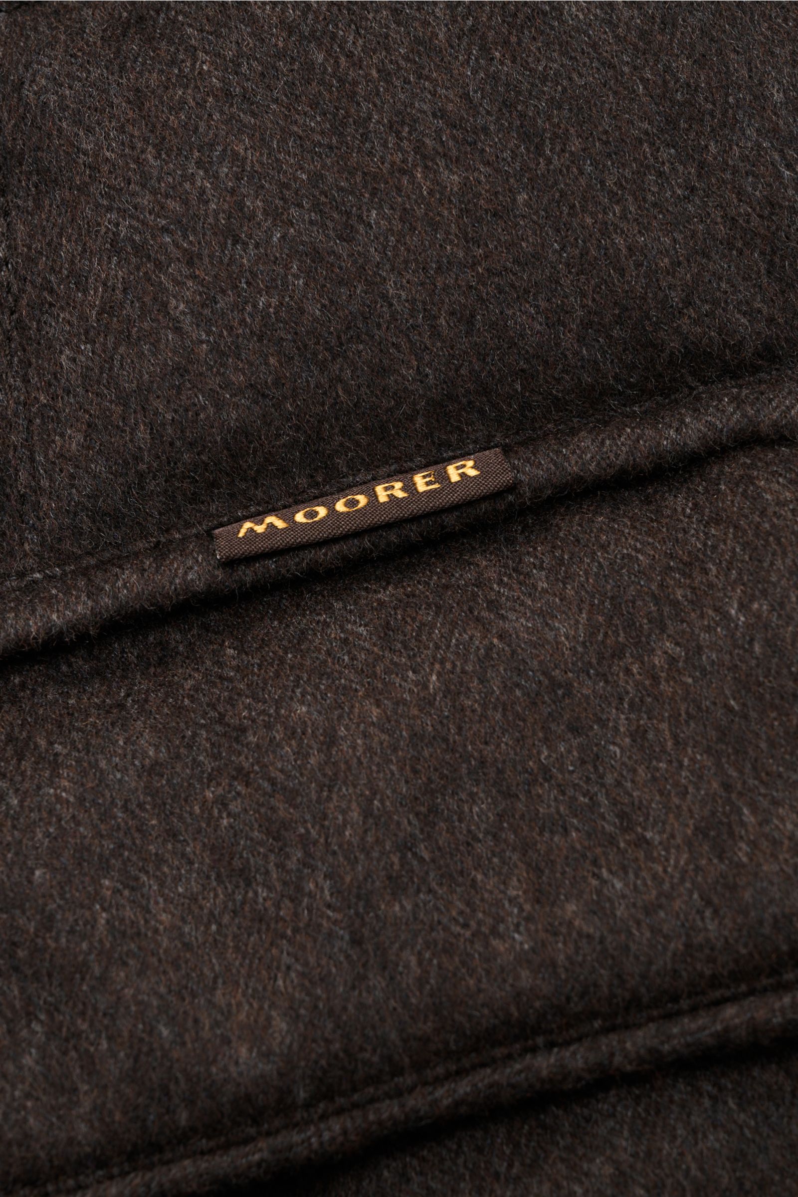 Nahaufnahme von der dunkelbraunen Moorer Daunenjacke 'Costanzo' aus Wolle-Cashmere-Mix mit markantem Steppmuster und MOORER-Label.