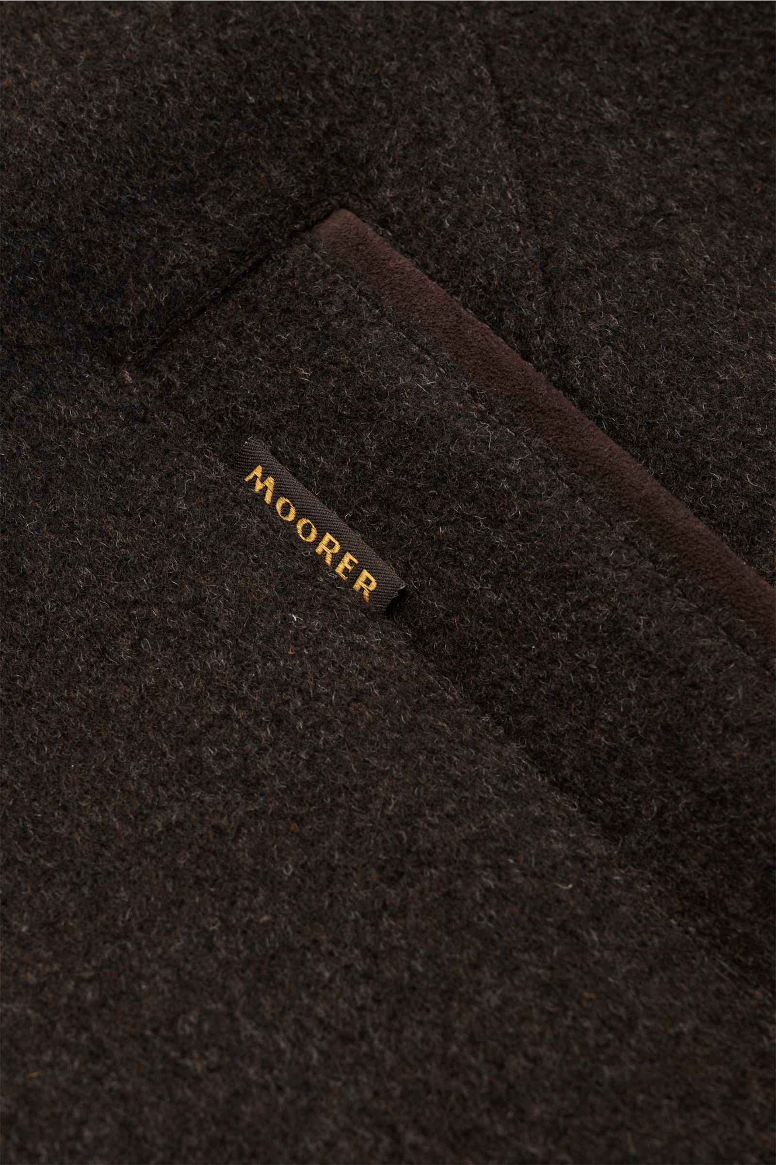 Nahaufnahme der Tasche und des MOORER-Labels der graubraunen Moorer Daunenjacke 'Teodor' aus Woll-Cashmere-Mix.