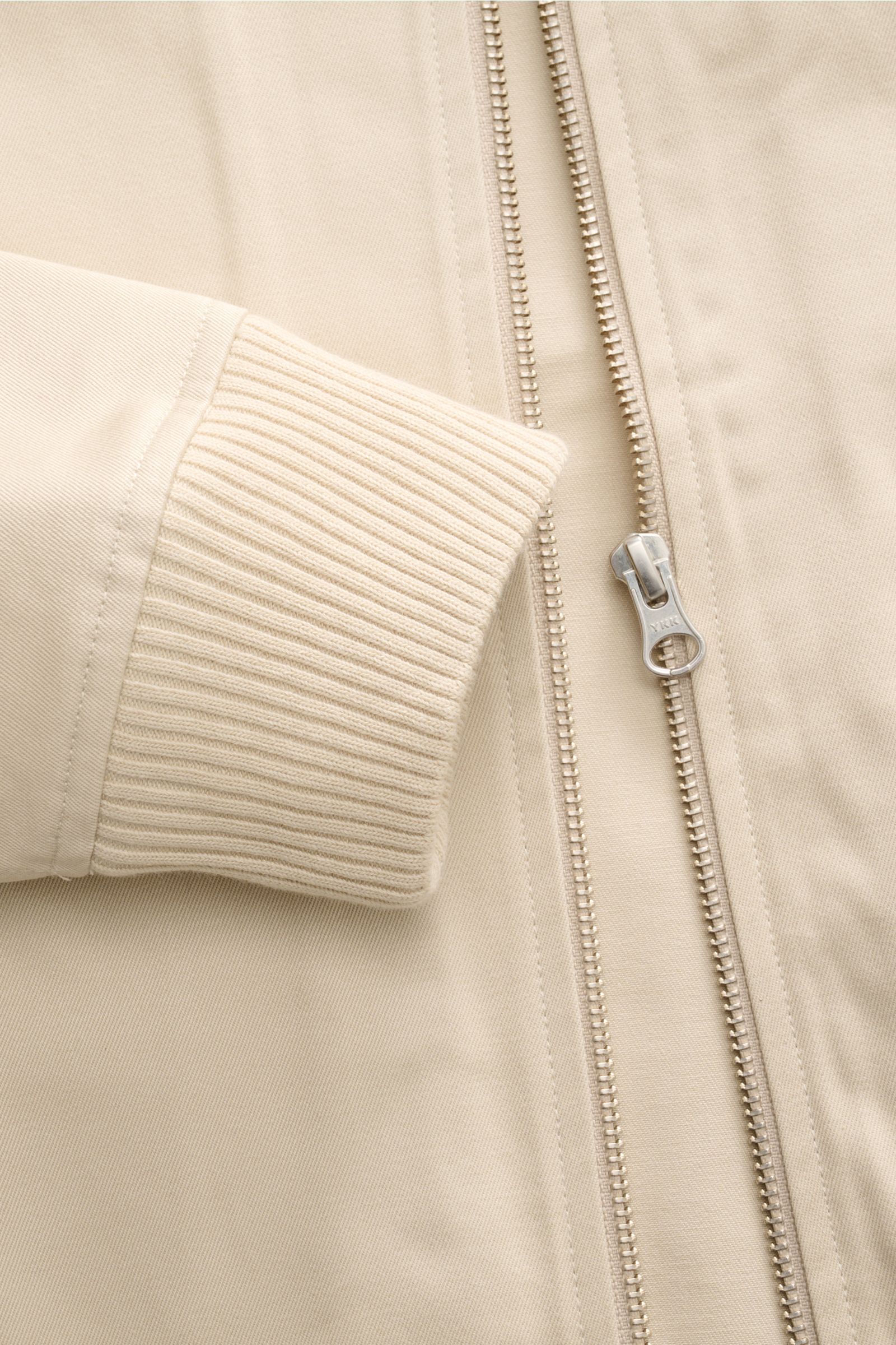 Close-up front view of the 04651/ A trip in a bag Blouson 'Griffin' beige showing ribbed elastic cuff, beige cotton fabric, and robust YKK zipper with unconstructed design. Souveräne Casual-Lässigkeit: Der Blouson von 04651/ A TRIP IN A BAG überzeugt mit 