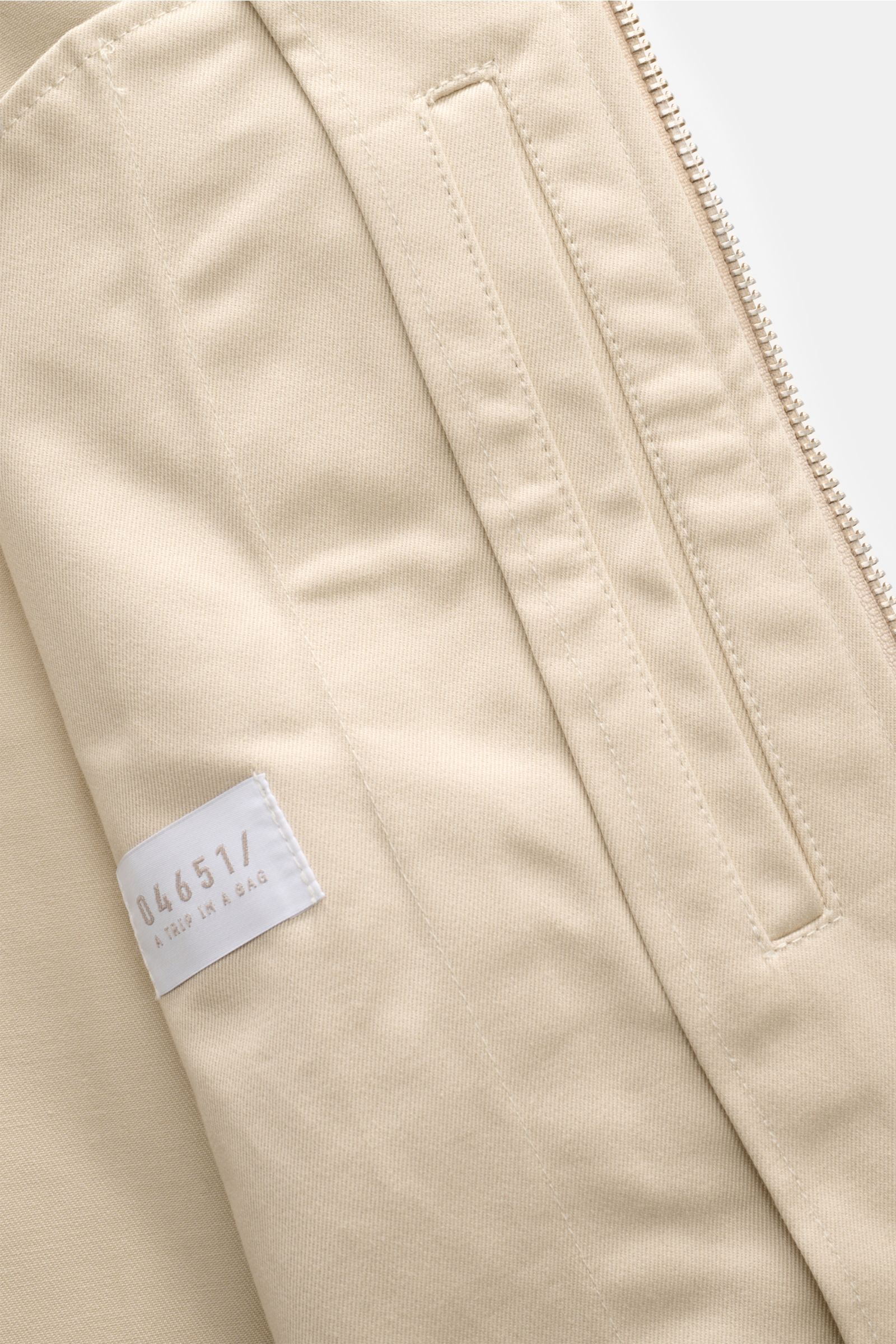 Close-up front interior view of 04651/ A trip in a bag Blouson 'Griffin' beige showing soft pure cotton fabric, robust zipper, piped front pocket, elastic cuffs, unconstructed design, and inside label.