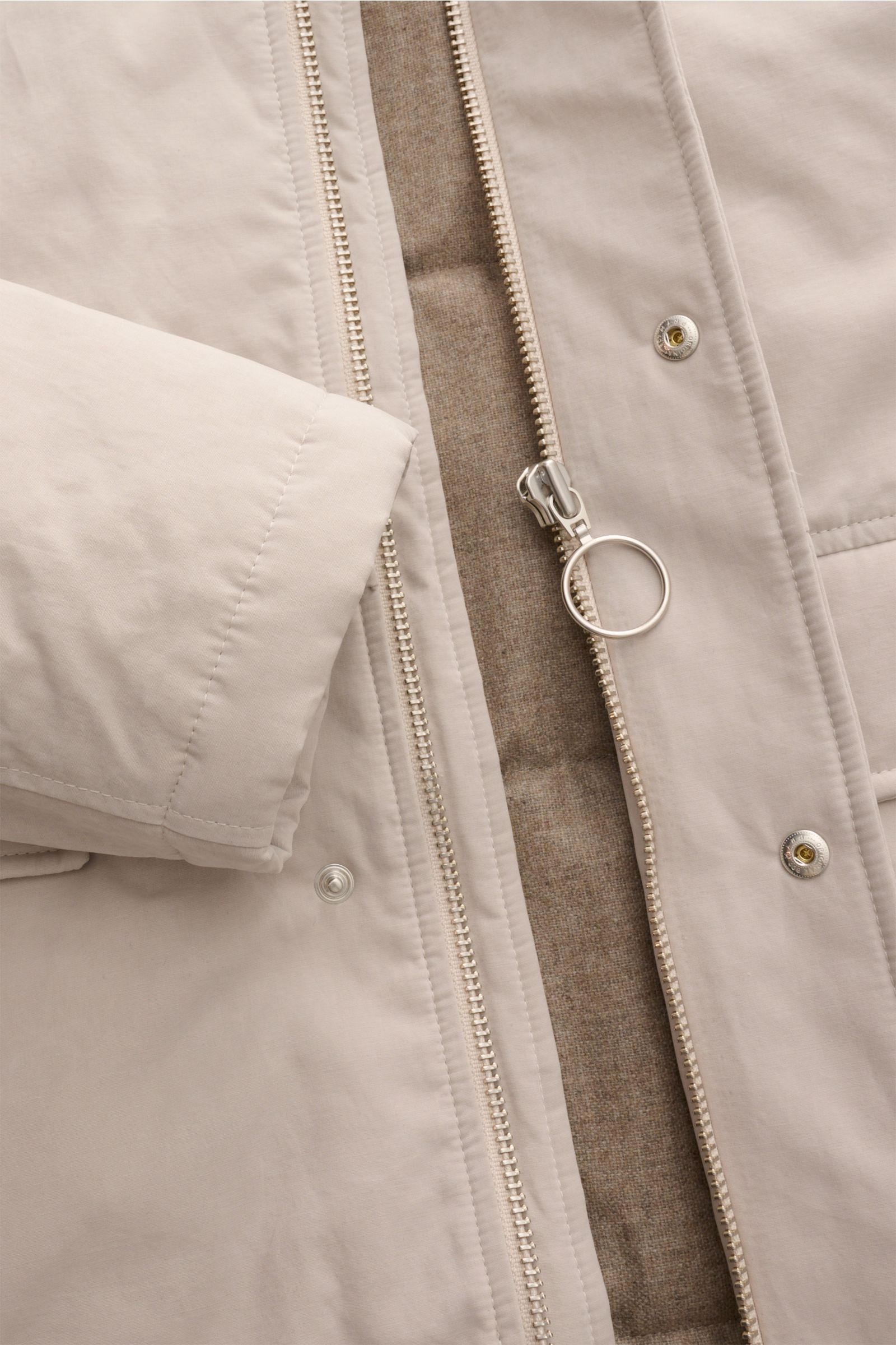 Close-up front view of the 04651/ A trip in a bag Parka 'MC26' sand, showing the sand-colored lightly waxed cotton fabric, two-way zipper with large ring pull, snap buttons, and warm wool-mix lining. Inspiriert von den Olympischen Winterspielen in Cort