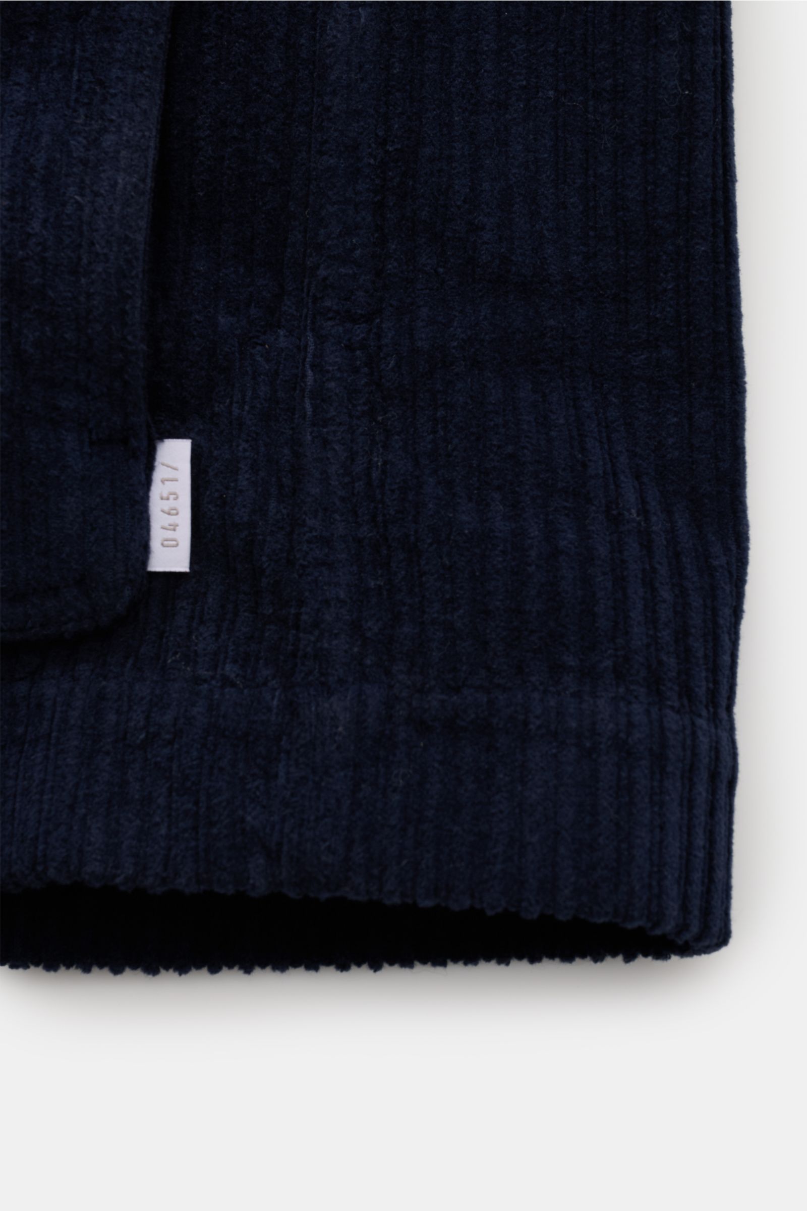 Close-up of the hem and label detail of the 04651/ A trip in a bag Corduroy pea coat navy, showing the soft, voluminous wide wale cotton corduroy fabric and ribbed cuff from a front-side perspective.