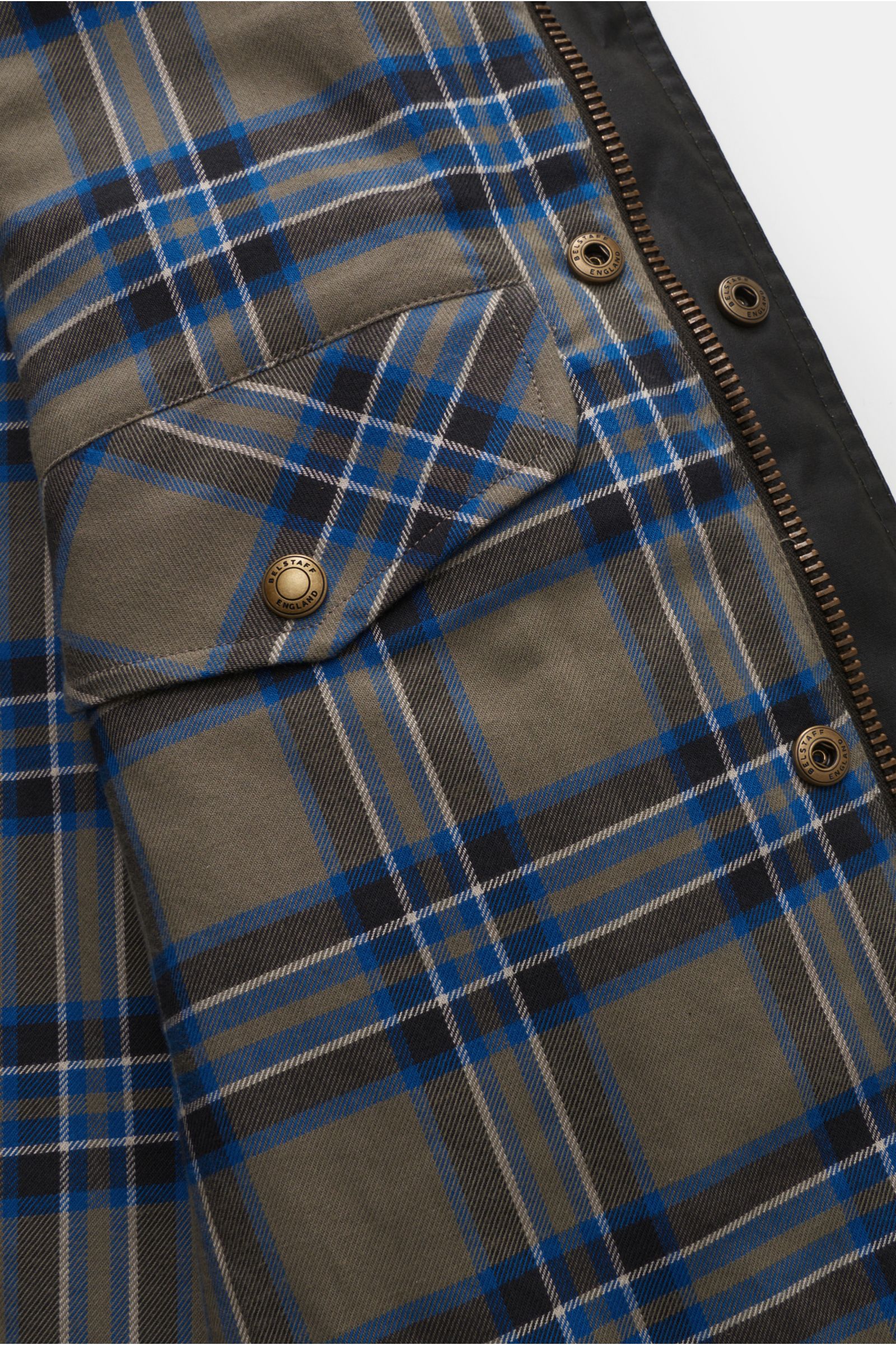 Close-up inside view of the Belstaff Wachsjacke 'Trialmaster' schwarz showing blue and grey plaid lining with branded snap buttons and zipper details.