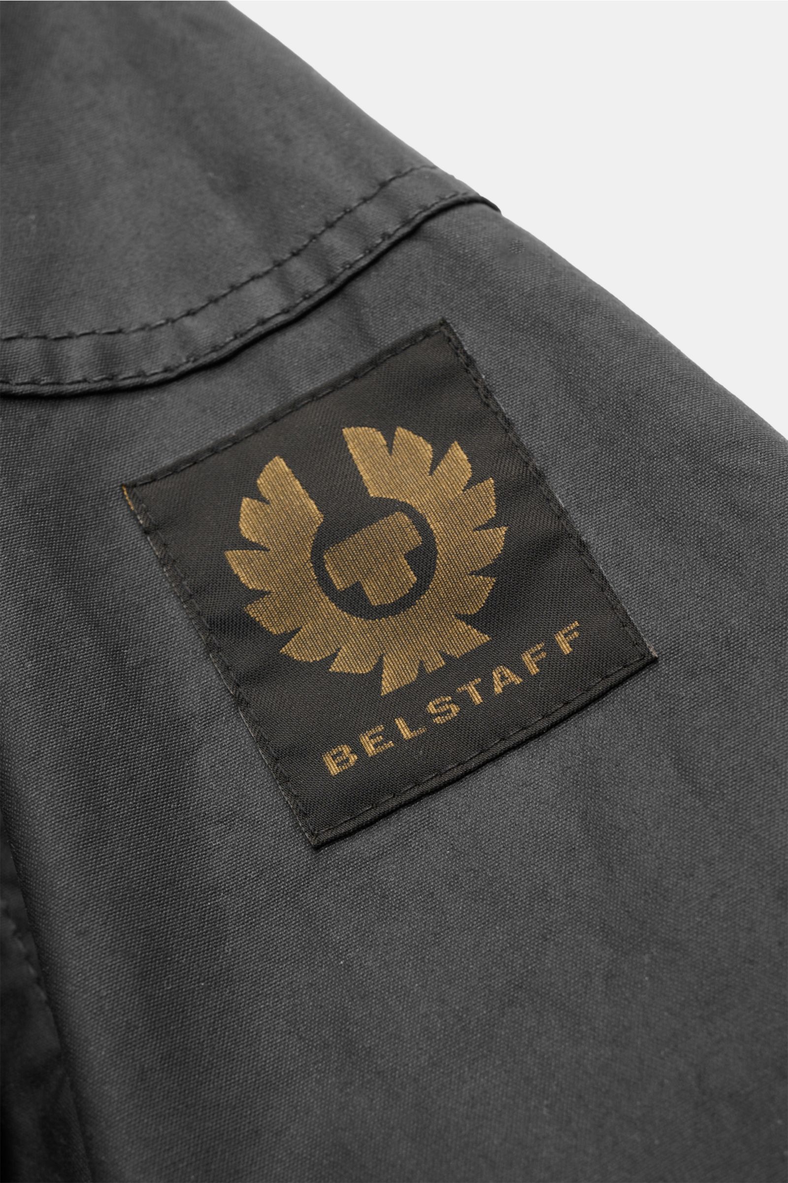 Belstaff Wachsjacke 'Racemaster' dark olive, Detailansicht des schwarzen BELSTAFF-Logos auf gewachster Baumwolle, robust und windabweisend.