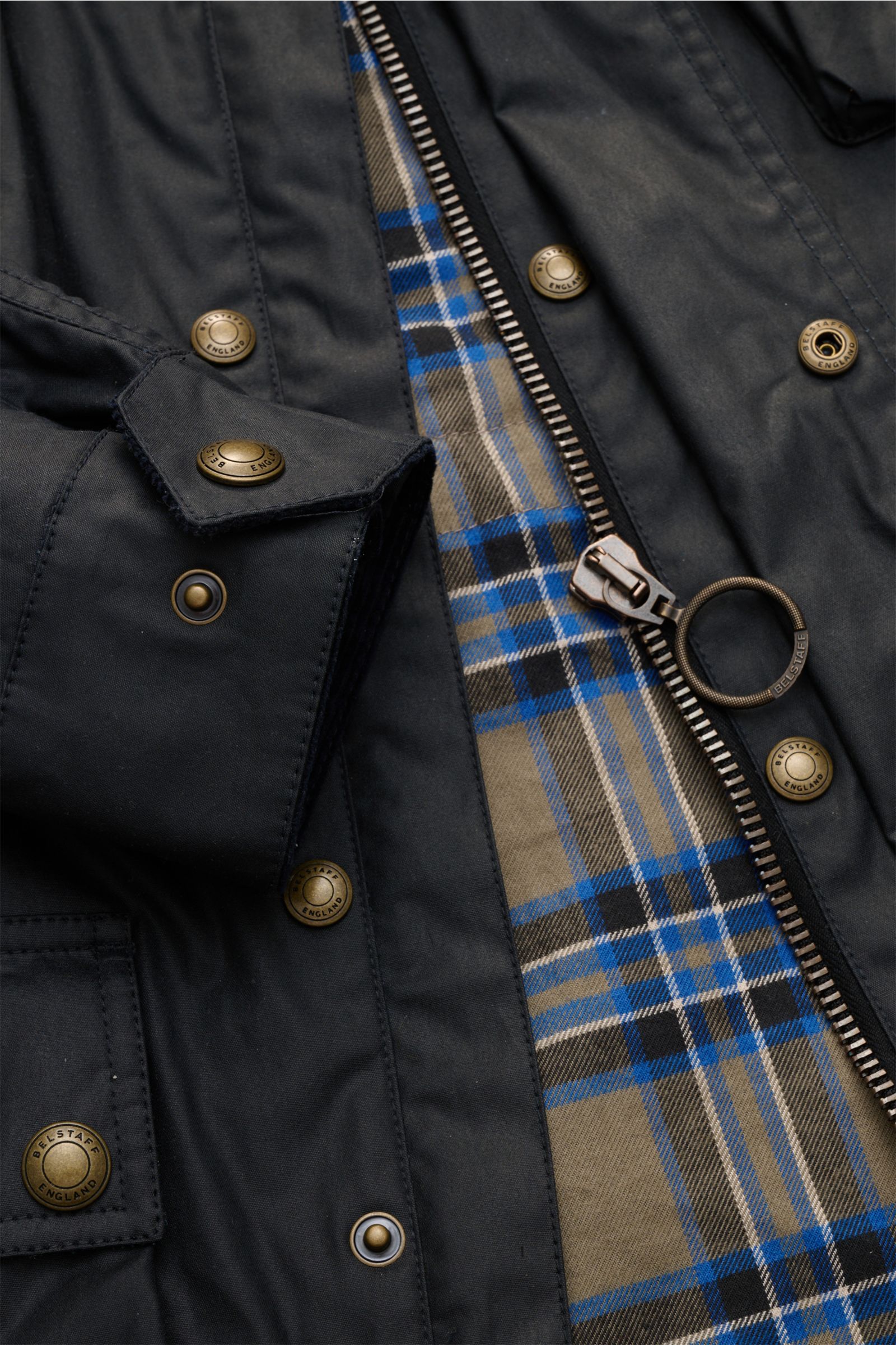 Nahaufnahme der Belstaff Wachsjacke 'Fieldmaster' dark navy mit gewachster Baumwolle, Metall-Reißverschluss, Druckknöpfen und karierter Baumwoll-Innenfütterung.